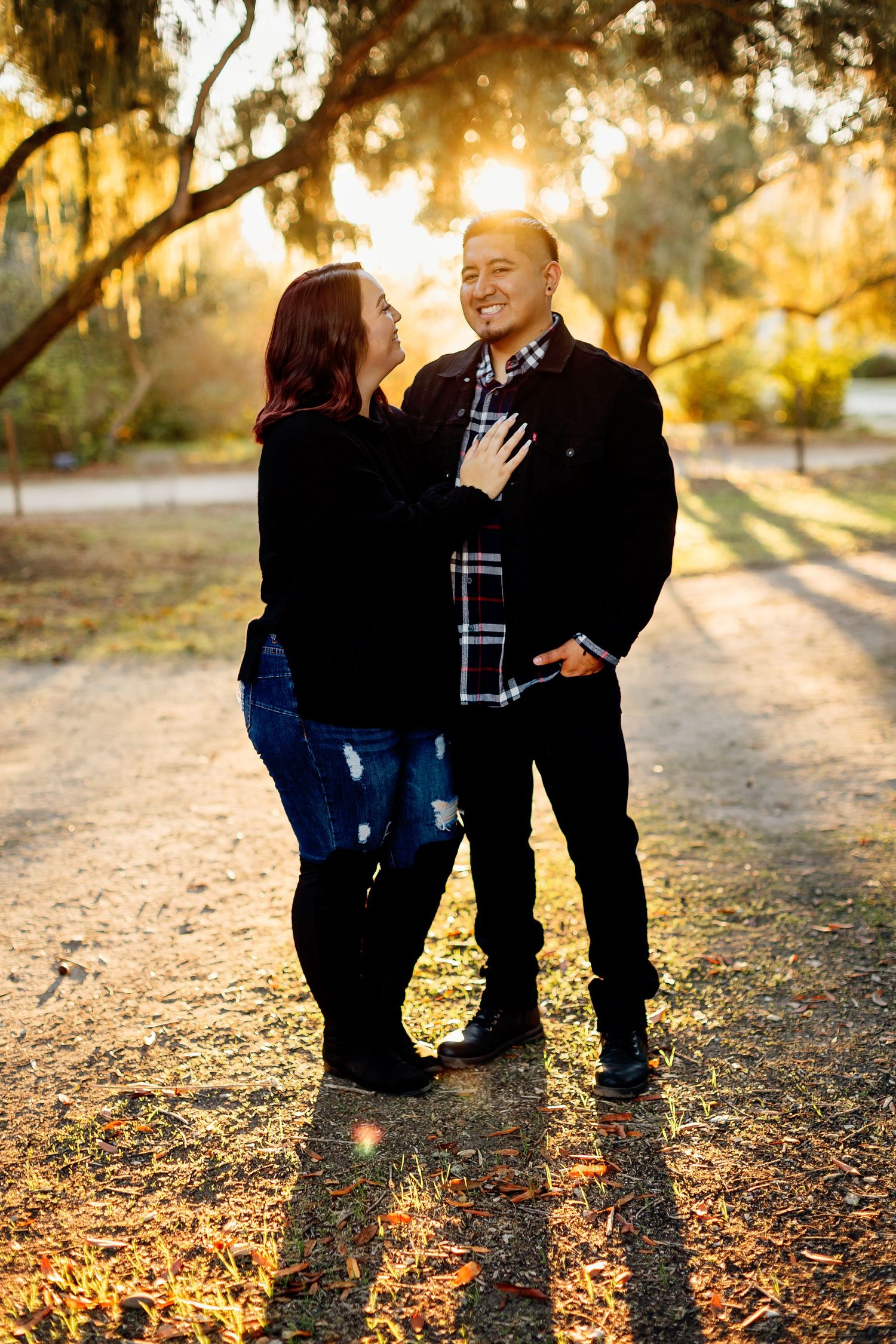 Two people sharing a tender moment in golden sunset light, surrounded by fallen autumn leaves and trees.