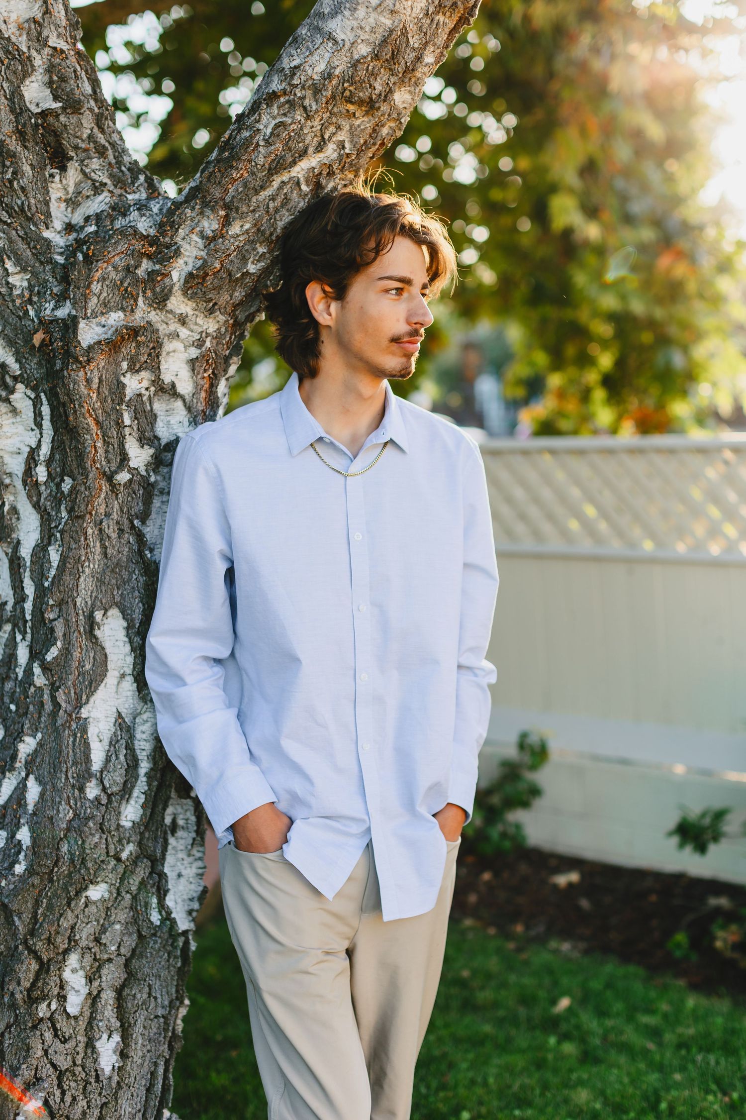 Person in light blue button-down shirt leaning against tree trunk in garden setting.