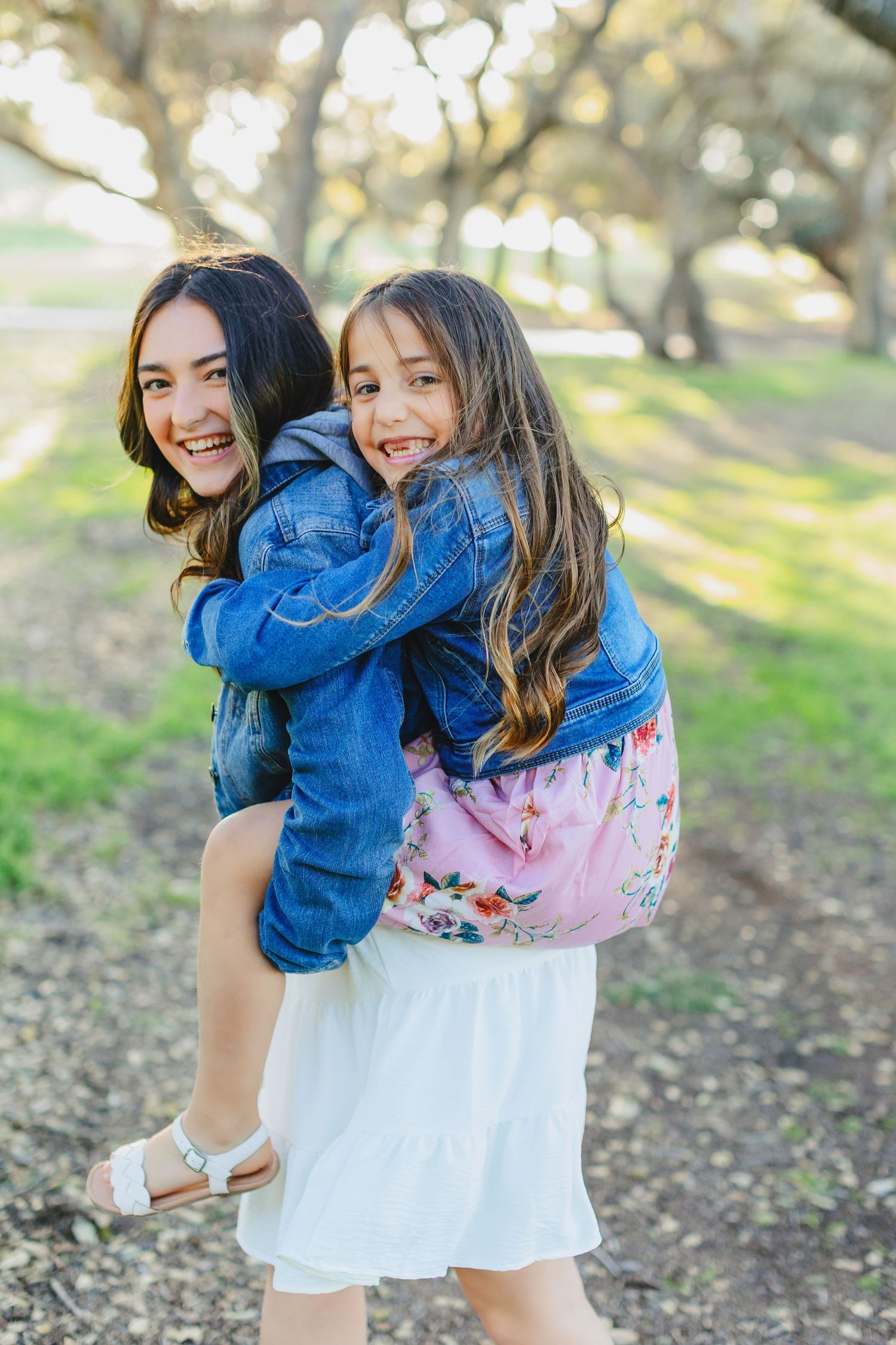 Joyful piggyback ride in a park with dappled sunlight streaming through trees.