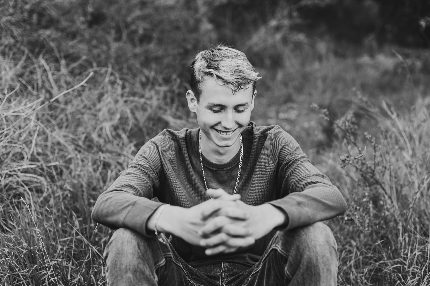 Young man smiling and sitting in a grassy field, black and white portrait photography outdoors.