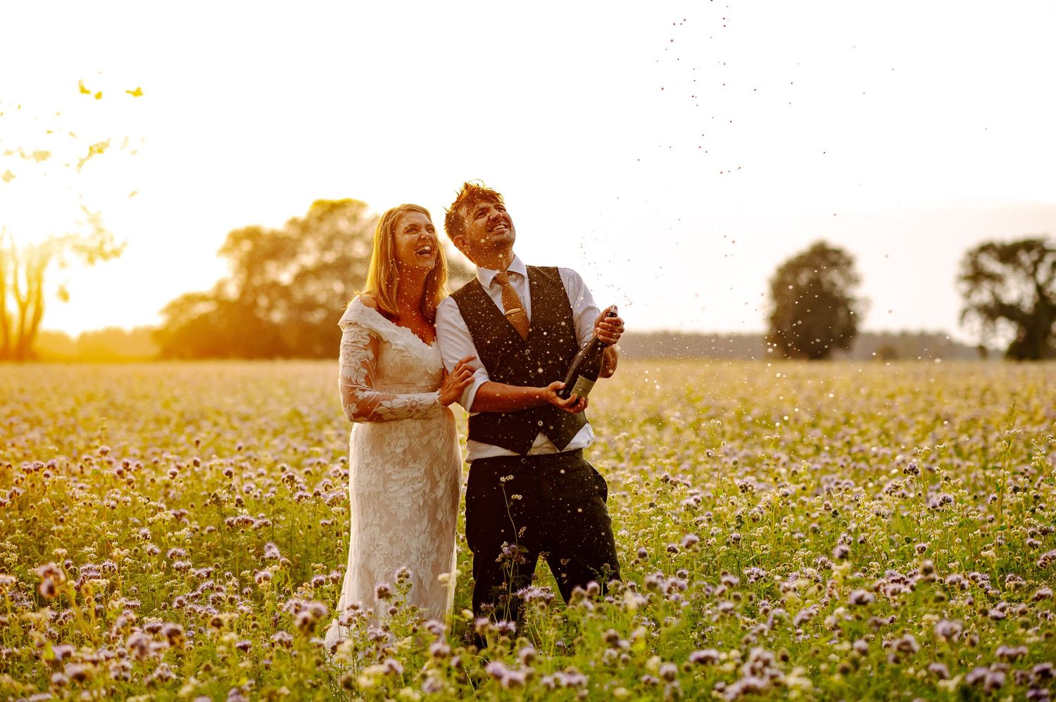 A couple stands together in a golden wildflower meadow at sunset.