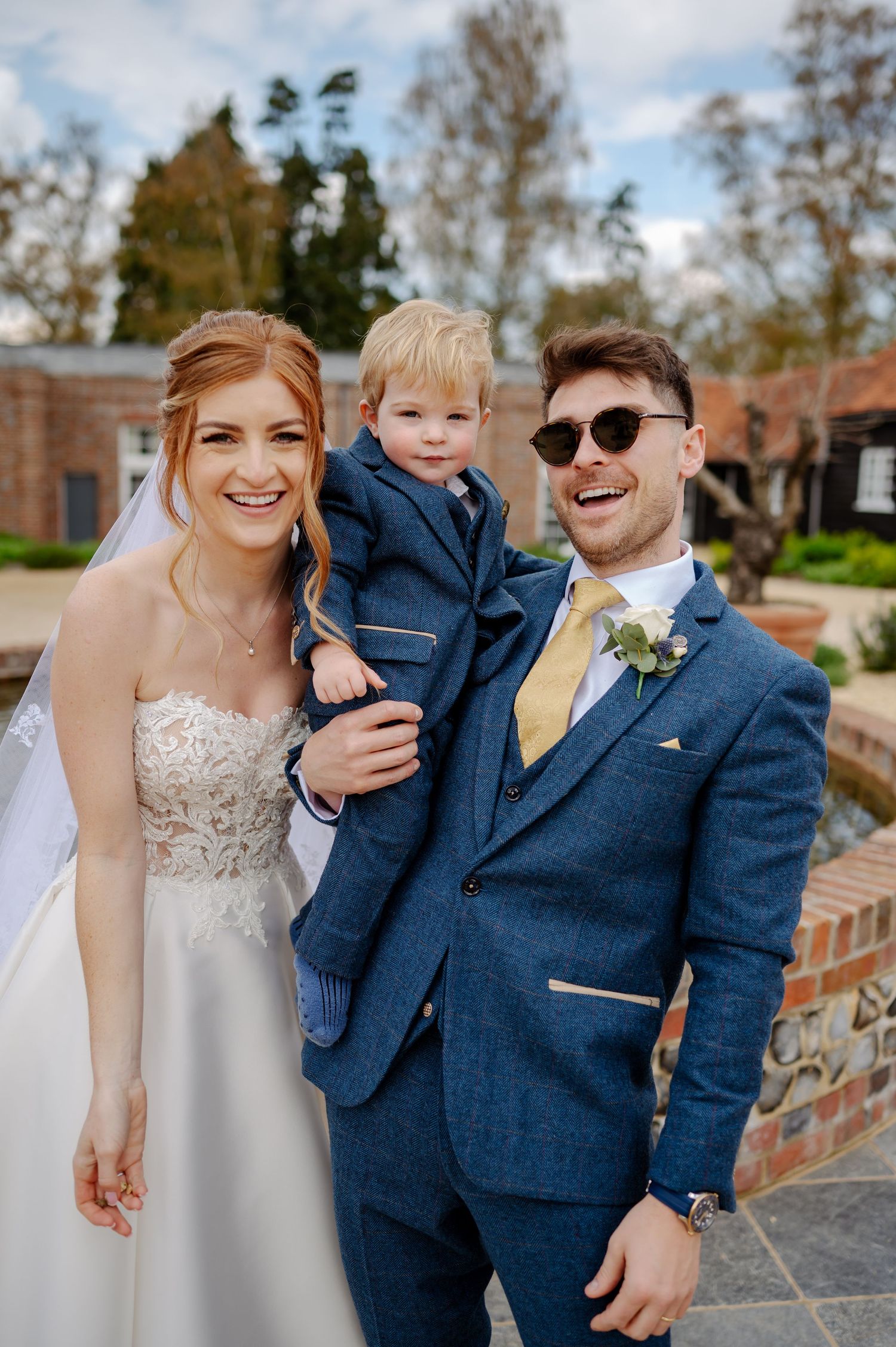 Wedding portrait of couple in formal attire with young child outdoors.