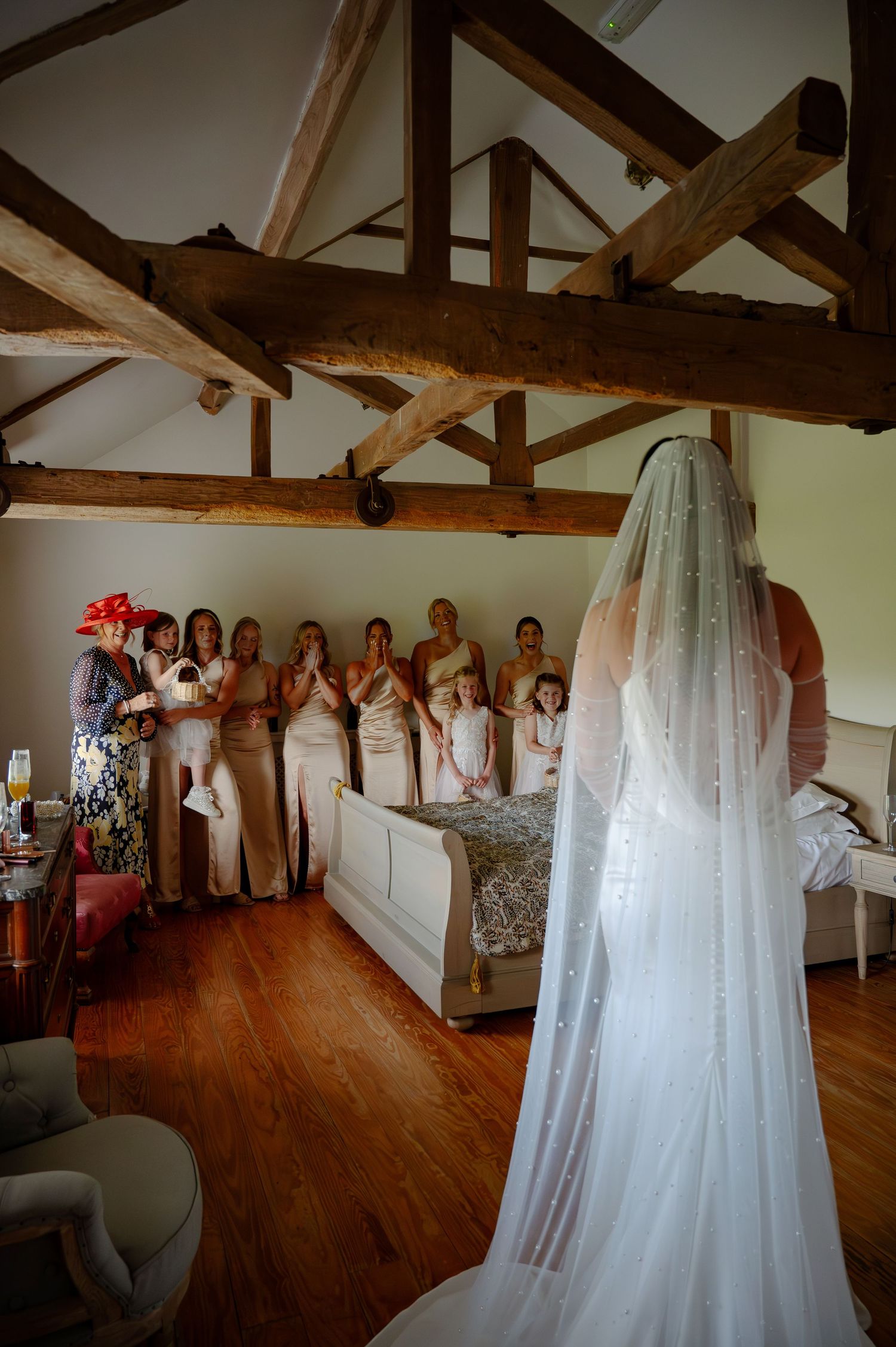 A wedding dress hangs elegantly in a rustic room with exposed wooden beams and hardwood floors.