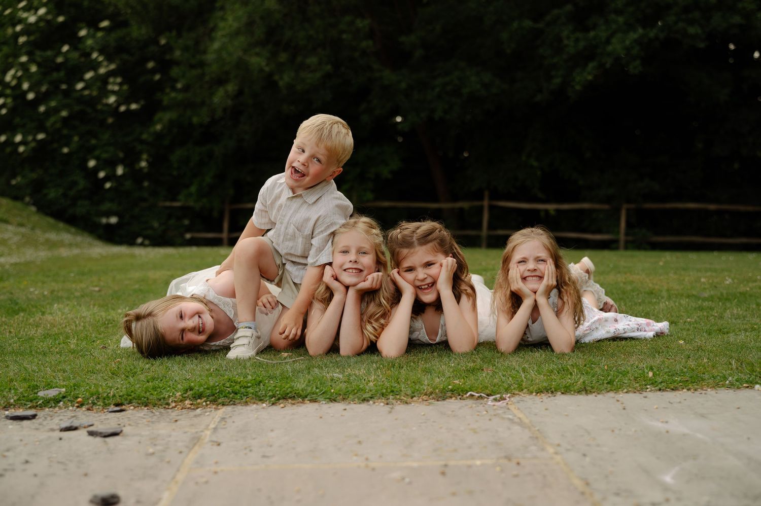 A group of people lying in a row on grass having fun during a casual outdoor photoshoot.