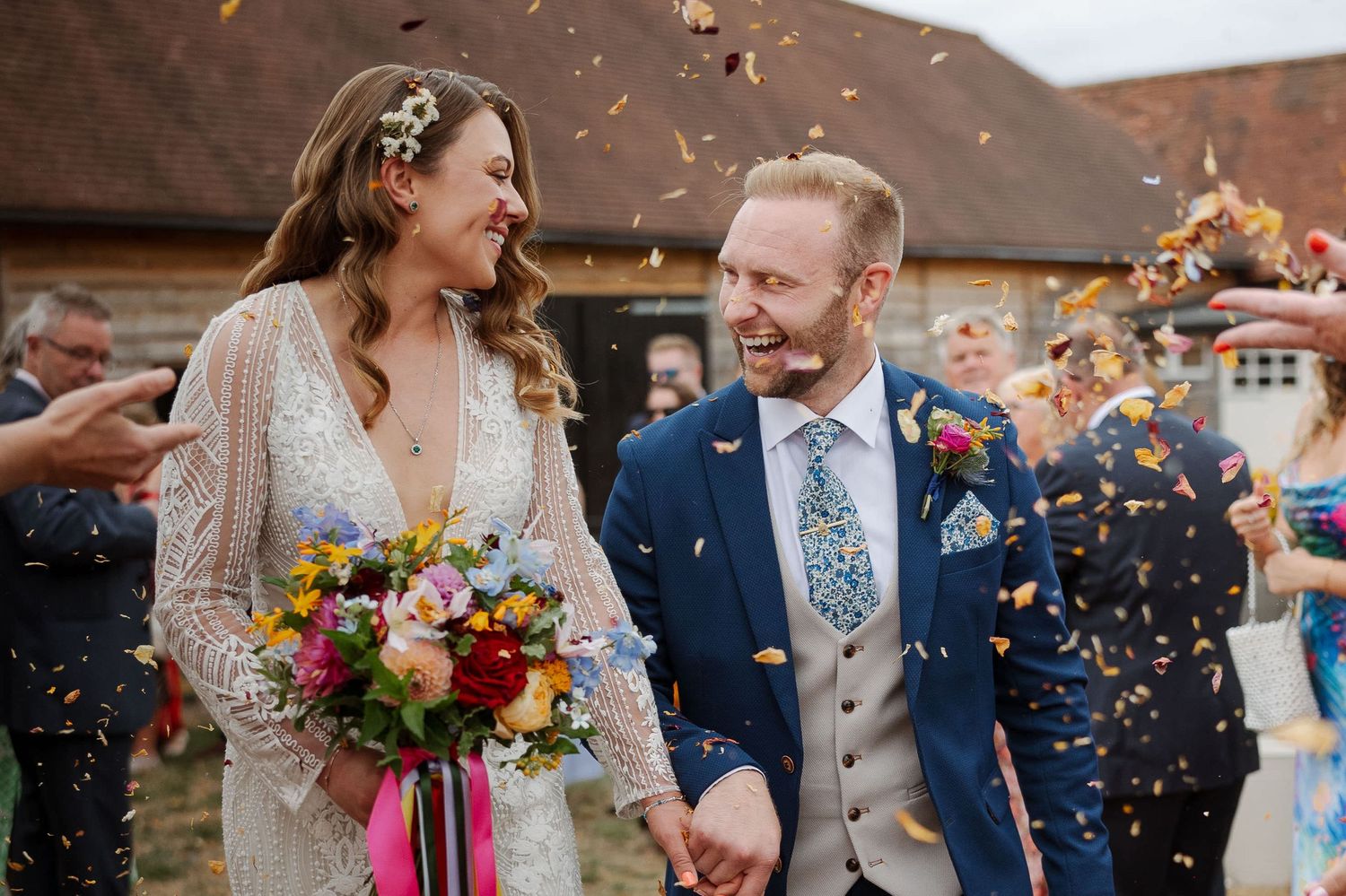 Newlywed couple celebrates with confetti during rustic outdoor wedding ceremony with colorful floral bouquet.
