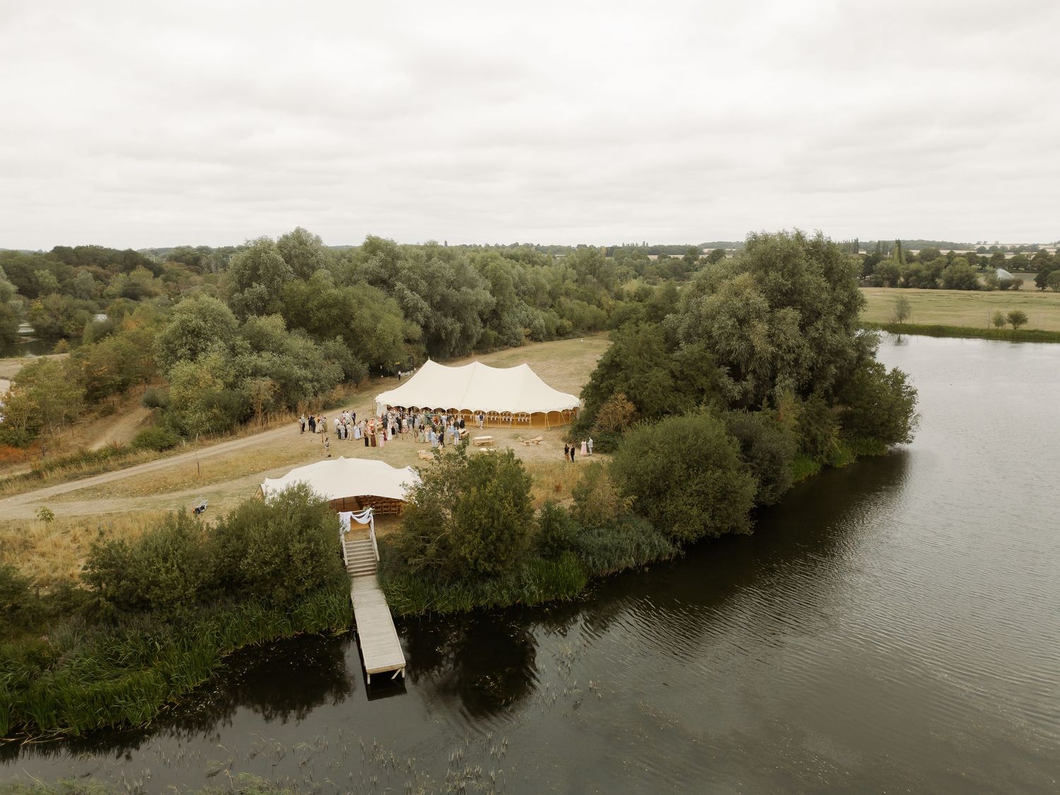 Aerial view of a wedding tent and dock setup on a scenic peninsula surrounded by water and trees.