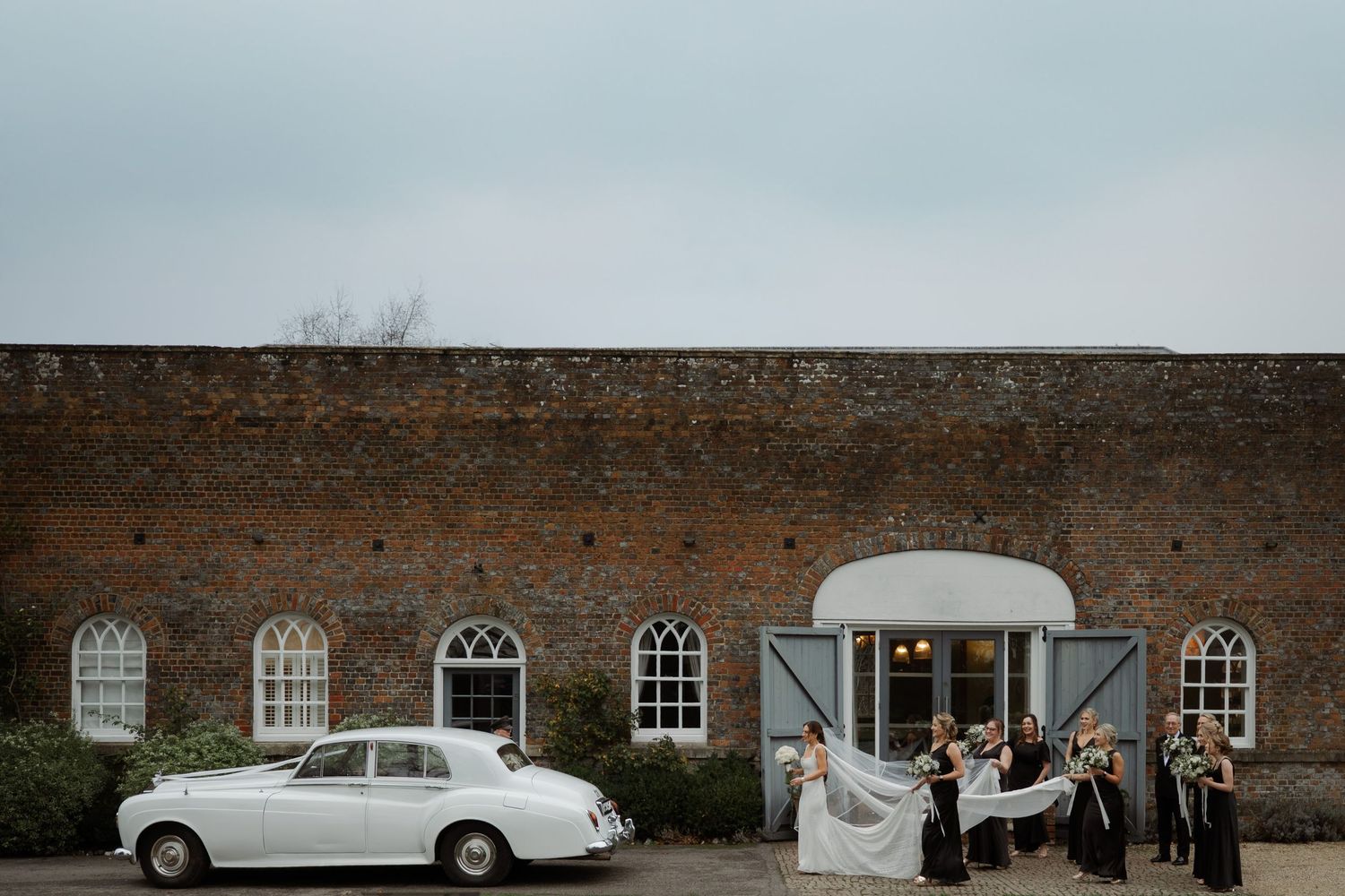 A panoramic view shows a rustic brick building facade with white-framed windows and a classic car parked outside.