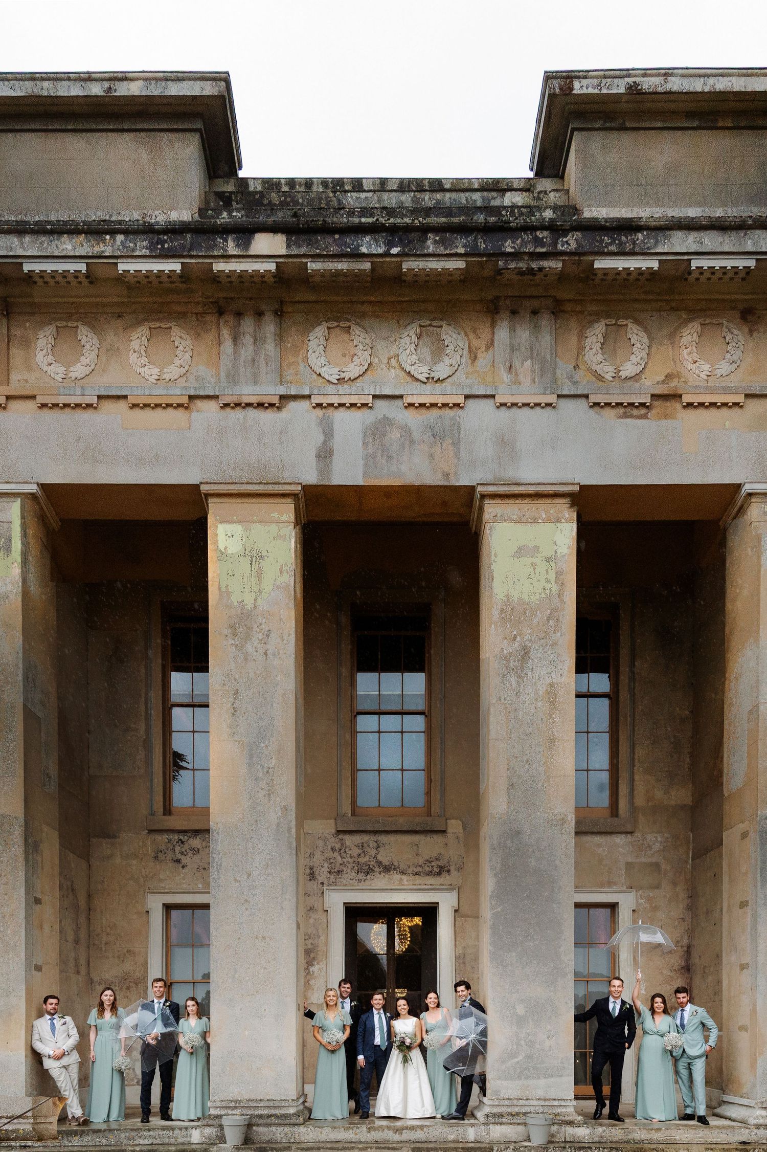 Wedding party poses on steps of grand neoclassical building with tall columns and ornate stone facade.