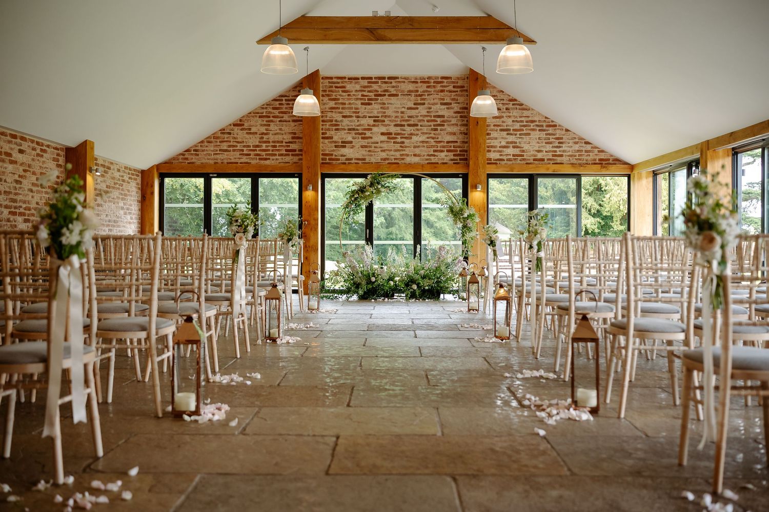 Elegant wedding ceremony venue with chiavari chairs, floral arch, stone floor, and vaulted brick ceiling flooded with natural light.