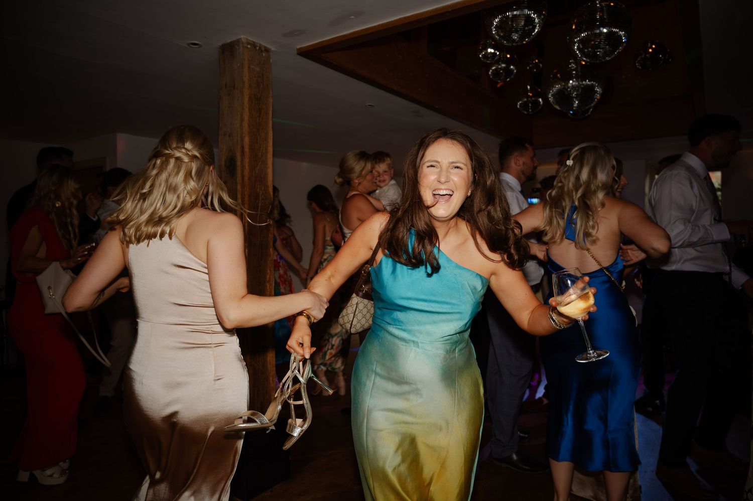 Wedding reception dance floor filled with guests dancing under dim lighting.