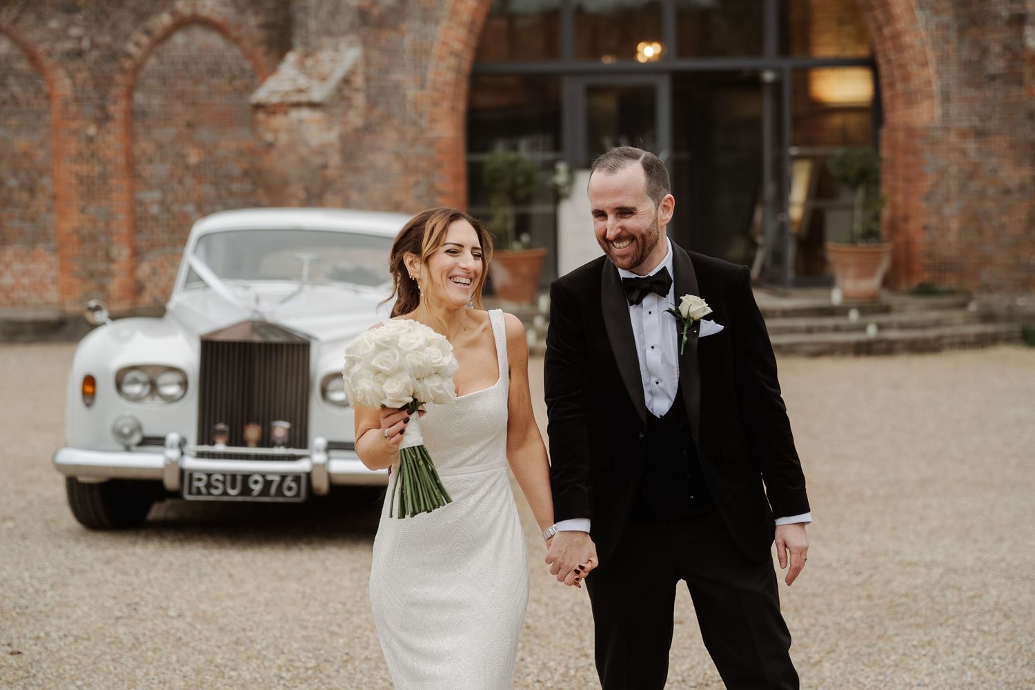 A bride and groom share a joyful moment while walking together on a rustic brick courtyard.