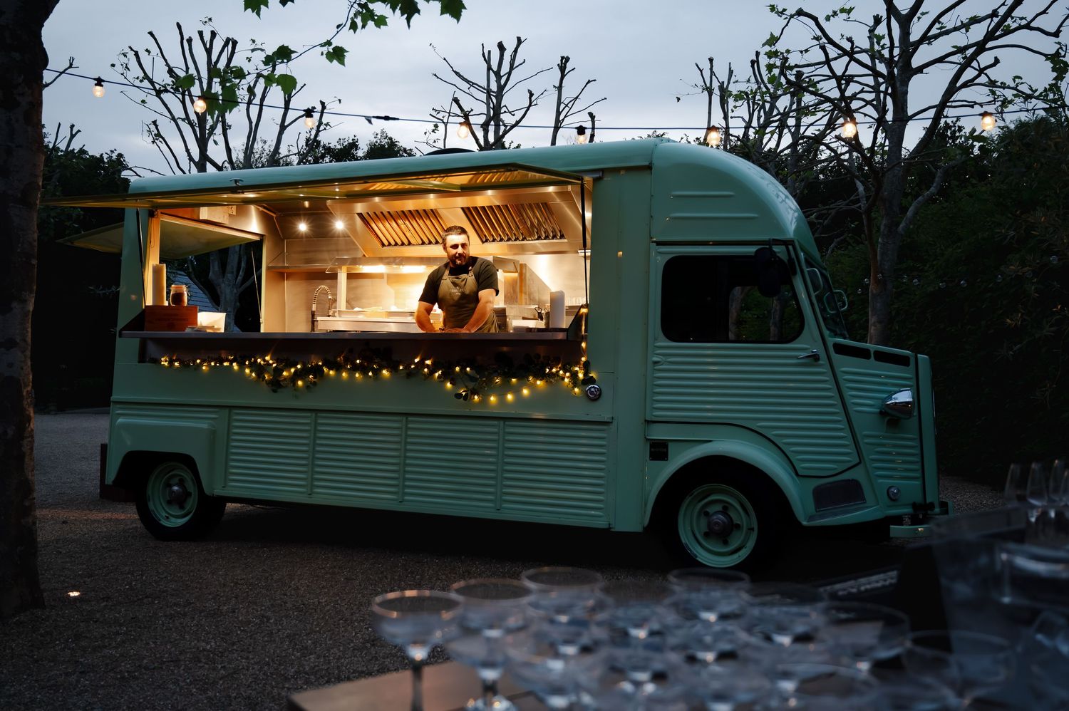 Vintage mint green food truck illuminated with string lights at an evening outdoor event.