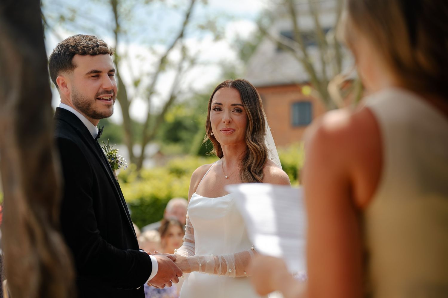 Wedding couple shares a joyful moment during their outdoor ceremony with guests looking on in the background.