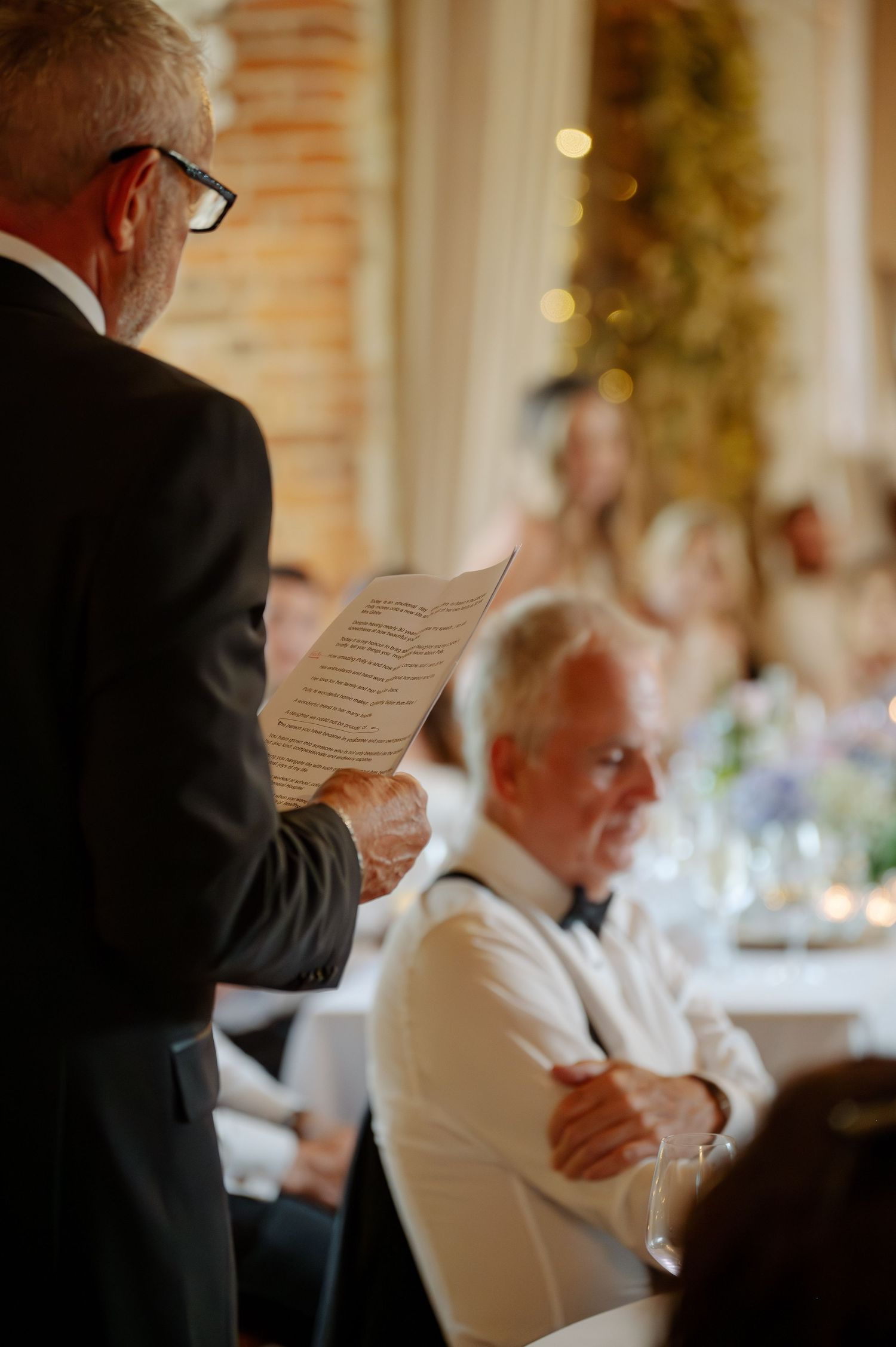 Wedding guests reading papers during an indoor reception with warm lighting.