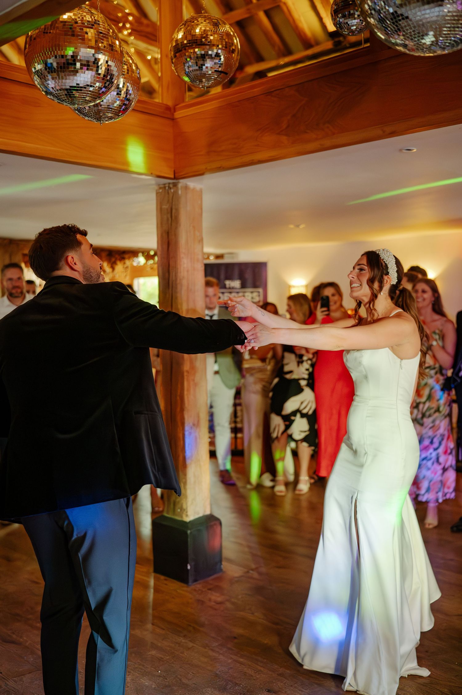 Wedding couple dancing and spinning on a wooden dance floor under disco balls and colorful lights.