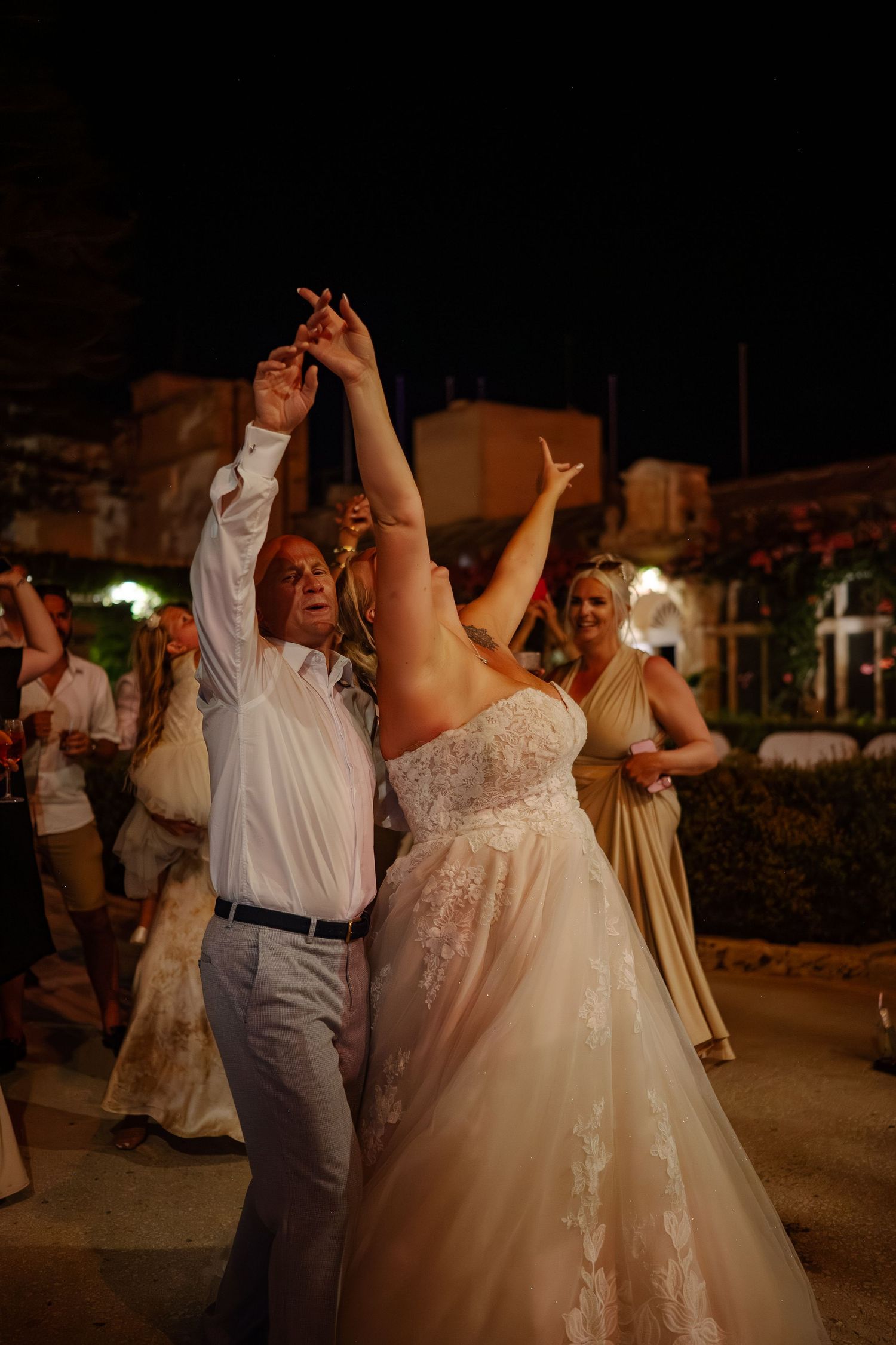 Wedding couple dances together at an outdoor evening reception as guests watch and celebrate.