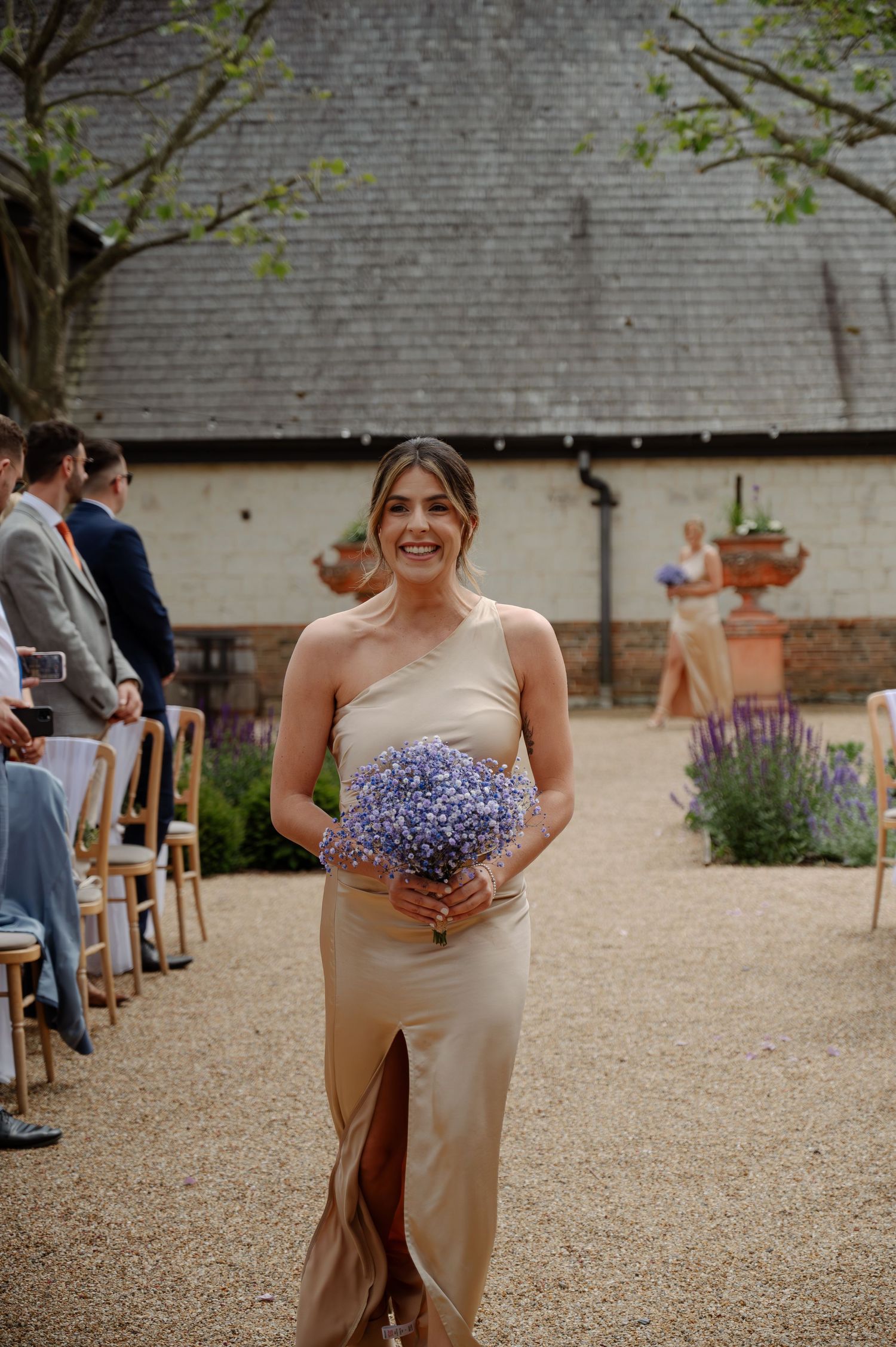 Bridesmaids in floral dresses walk down a gravel path at an outdoor wedding venue.