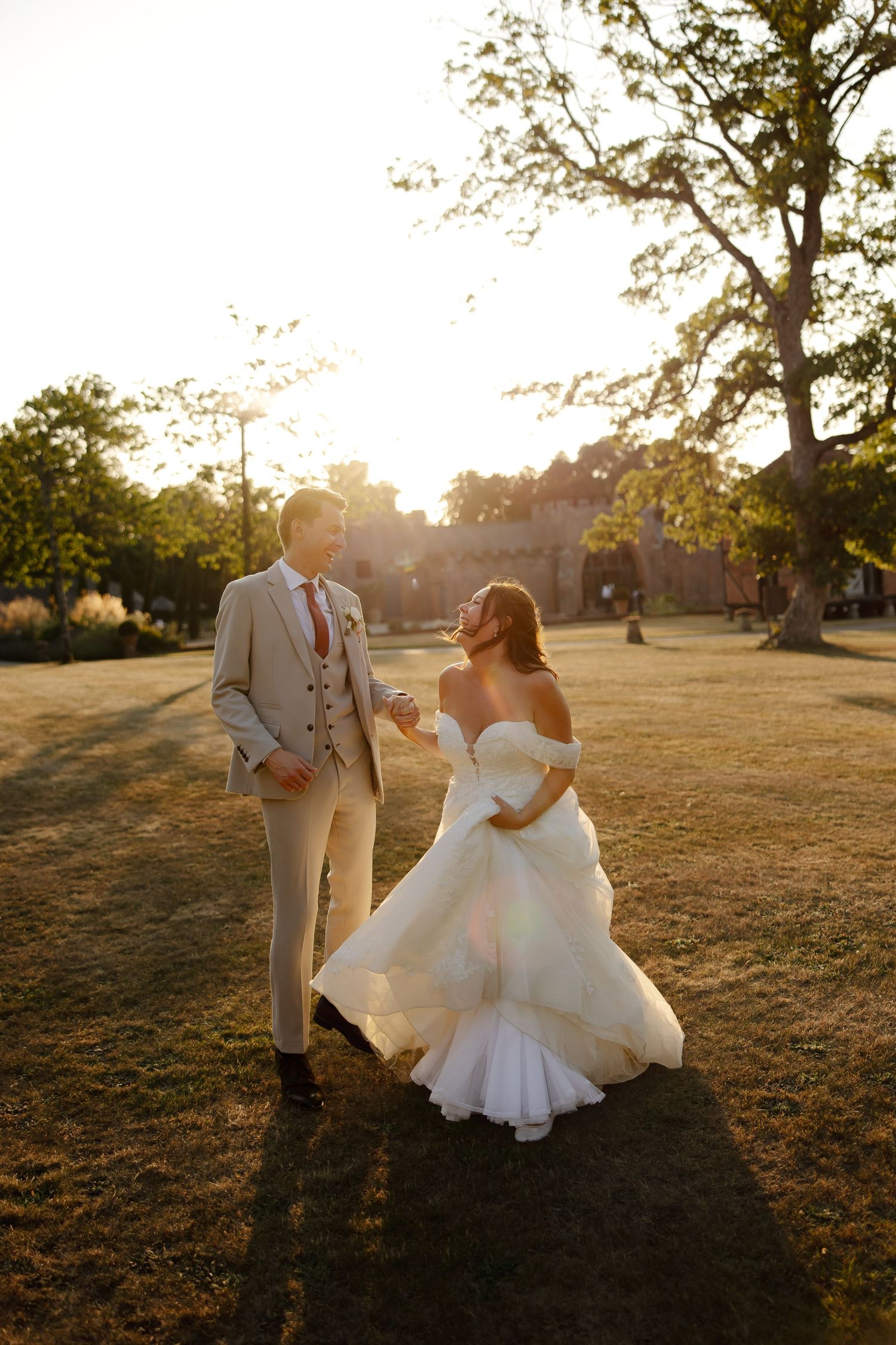 Newlywed couple dances together in a golden sunlit field during sunset, creating a romantic silhouette against the warm sky.