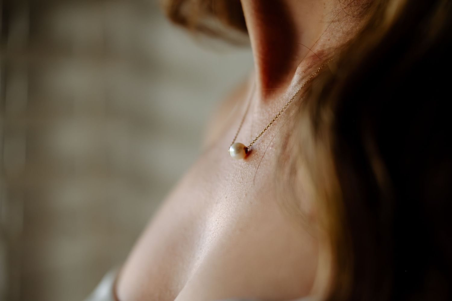 A delicate gold pendant necklace with a small heart charm hangs against a light background.