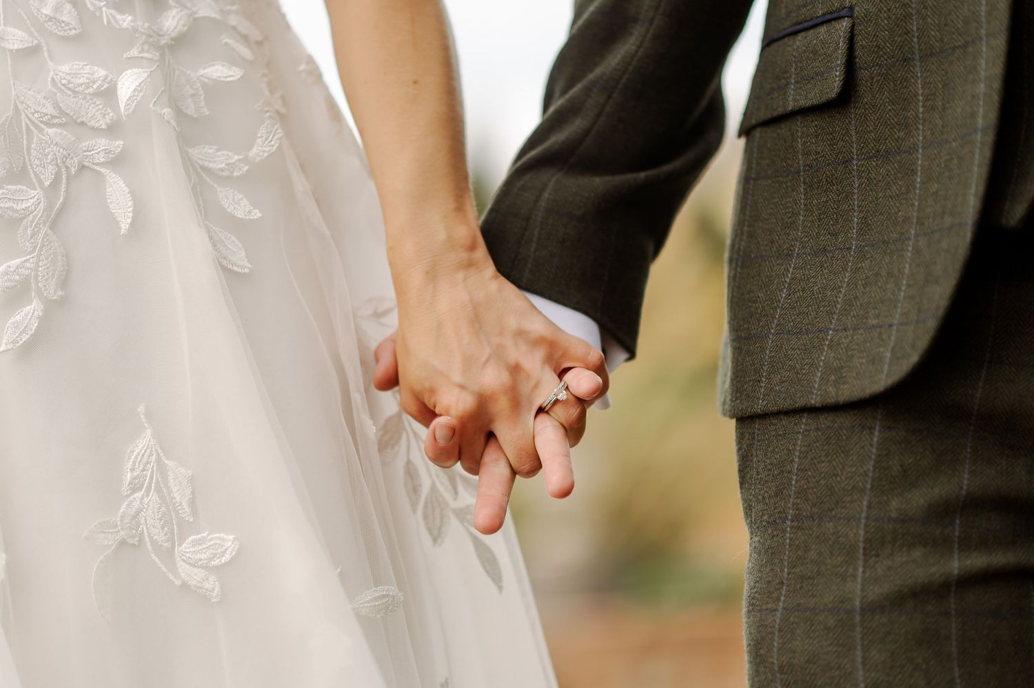 Bride and groom holding hands, wedding rings visible, bride in lace dress.