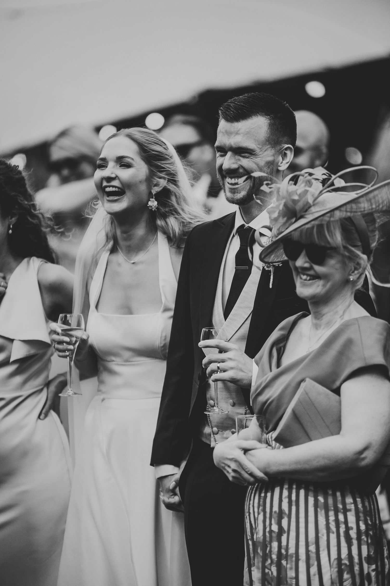 Black and white photo series showing wedding guests laughing and enjoying champagne at an outdoor celebration.