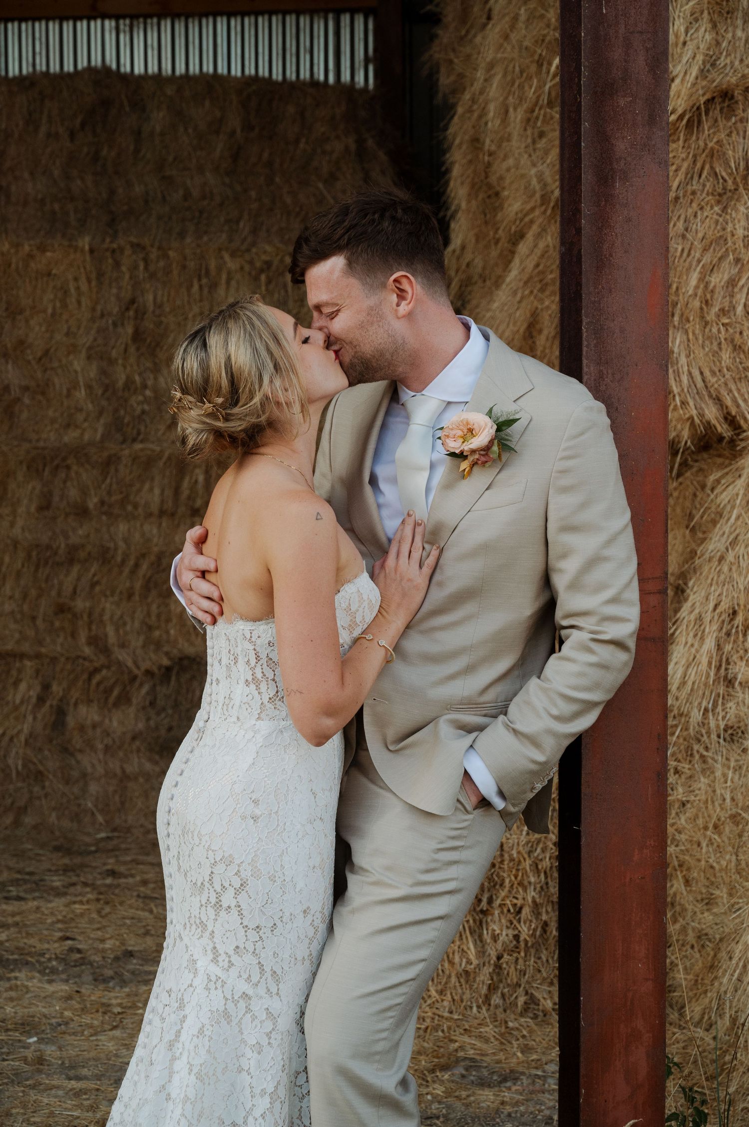 A romantic moment captured between newlyweds against a rustic barn wall with stacked hay bales in the background.