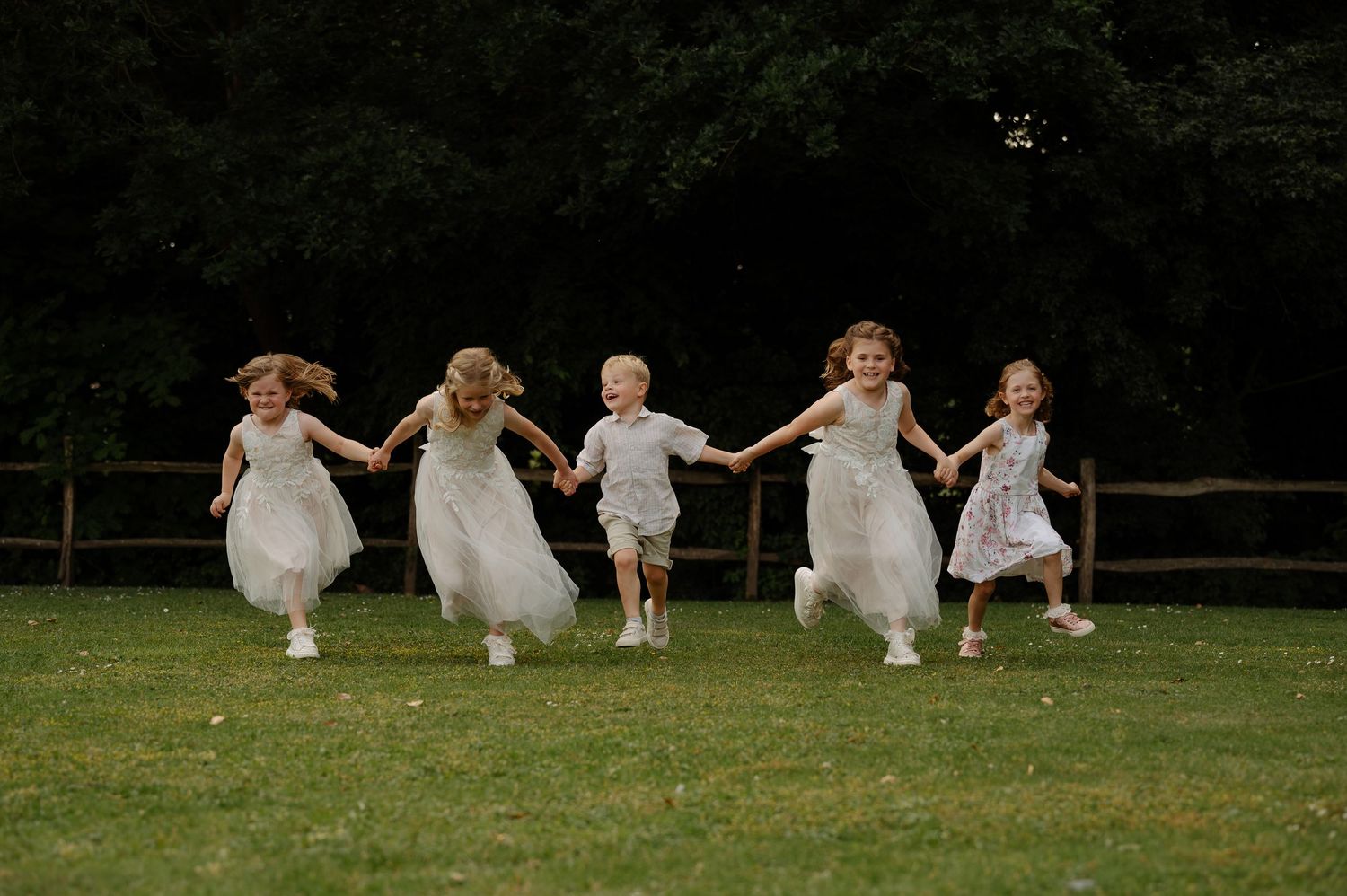Group running and jumping playfully on a grassy field in white dresses.