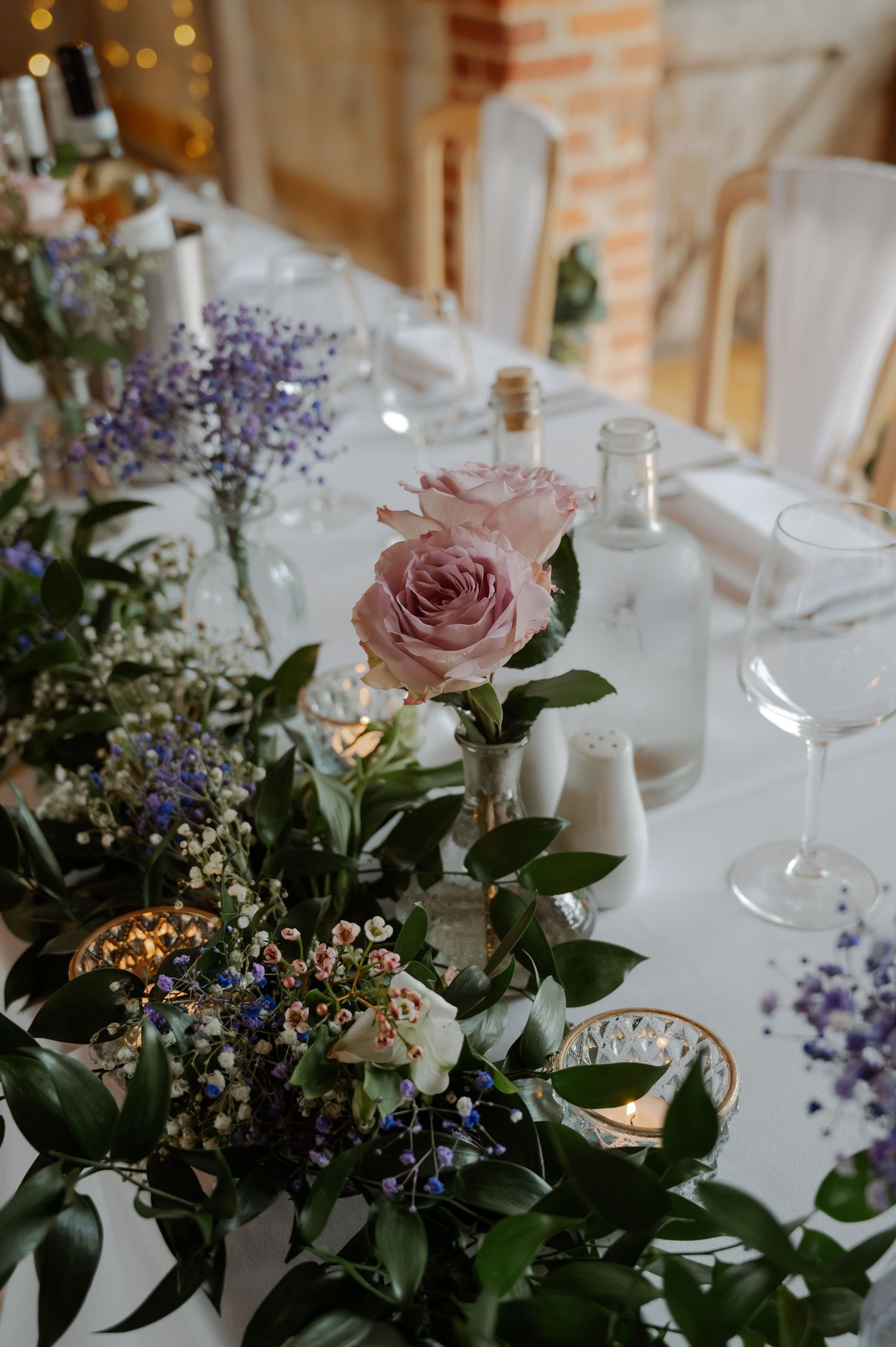 Elegant wedding table settings with pink roses, purple flowers, and white candles create a romantic atmosphere.