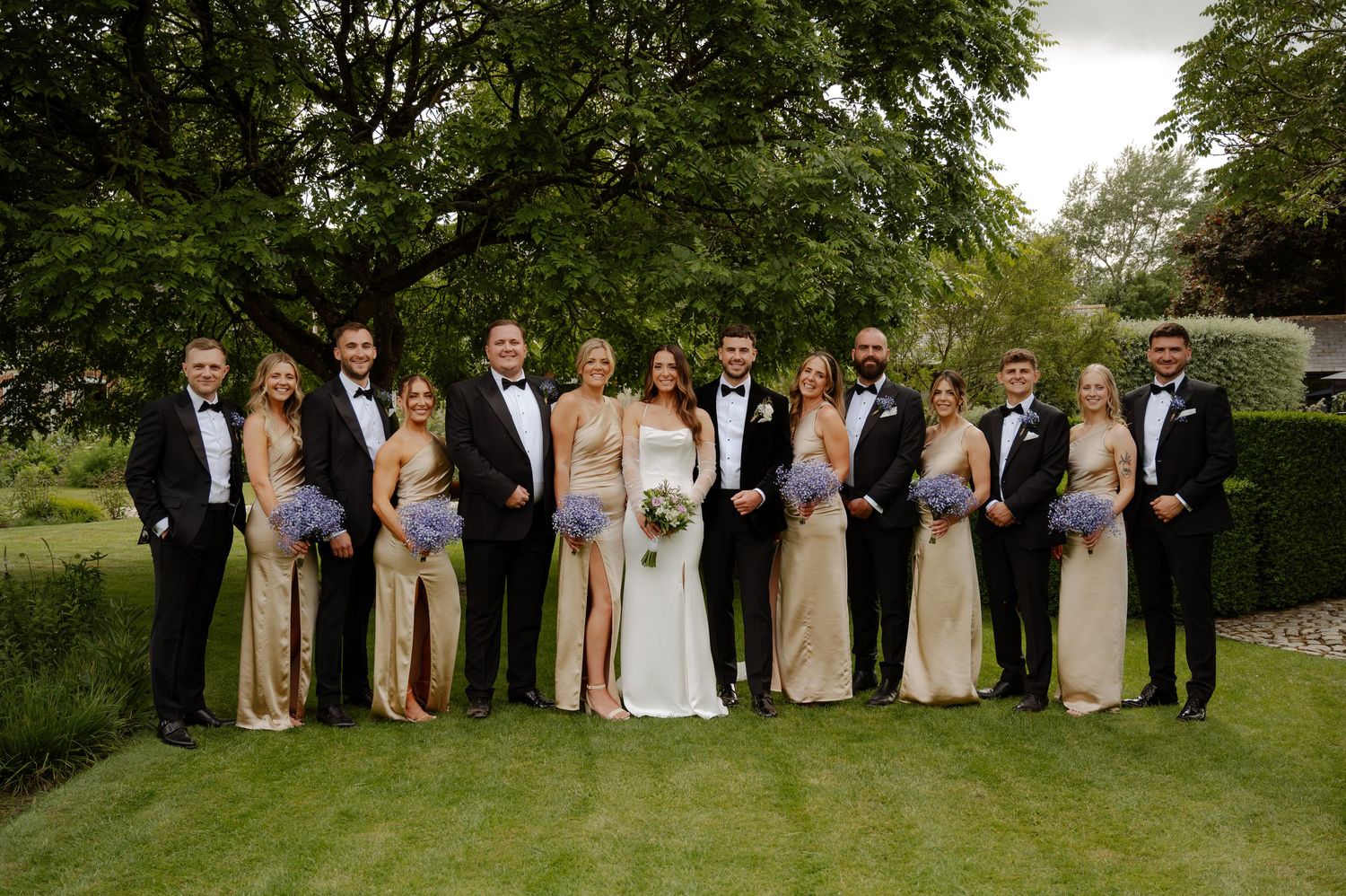 Wedding party poses together on a lush green lawn for formal group portraits.