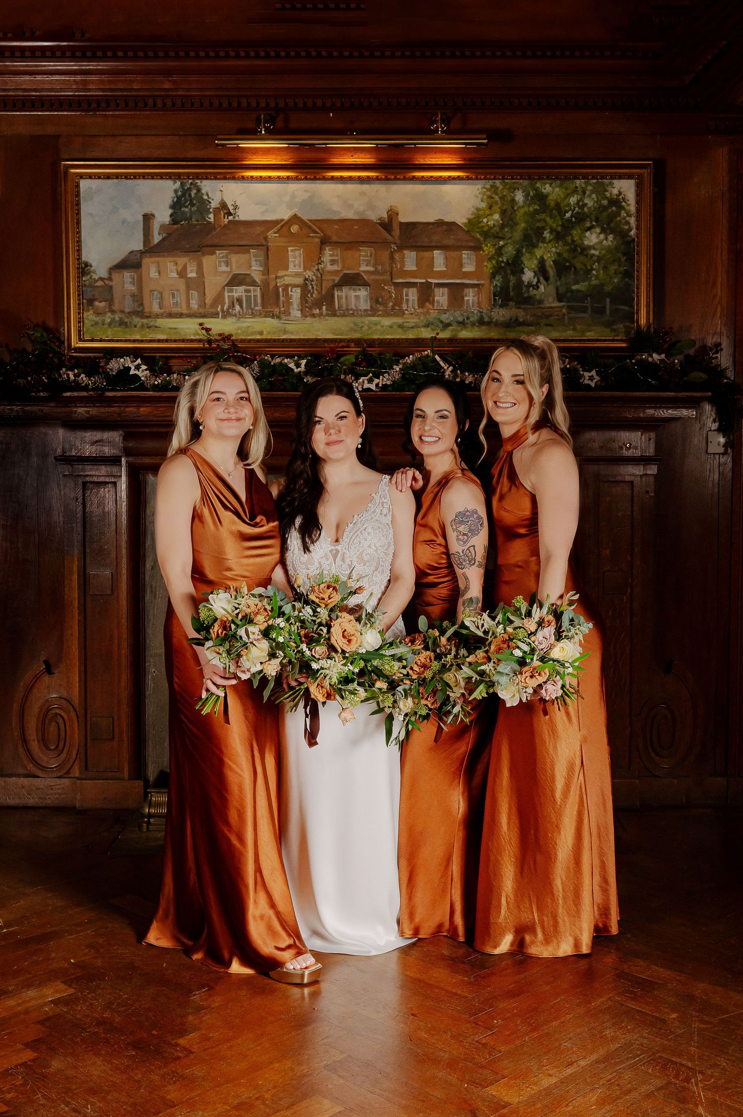 Bridal party in copper satin dresses poses with bouquets in elegant wood-paneled room.