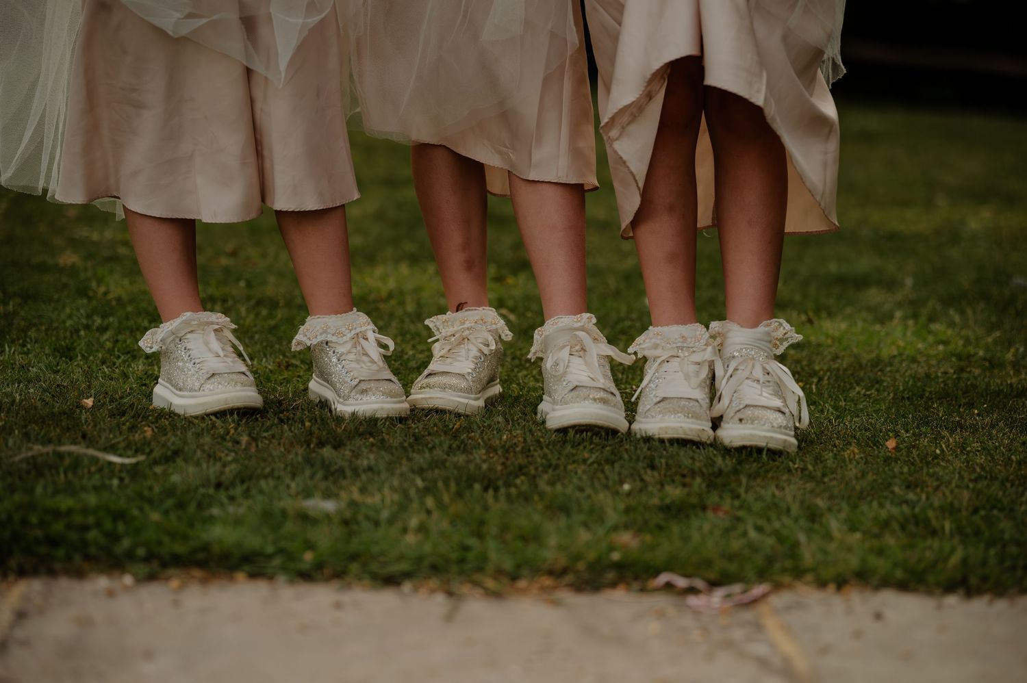 Row of wedding guests' feet in casual shoes lined up on grass.