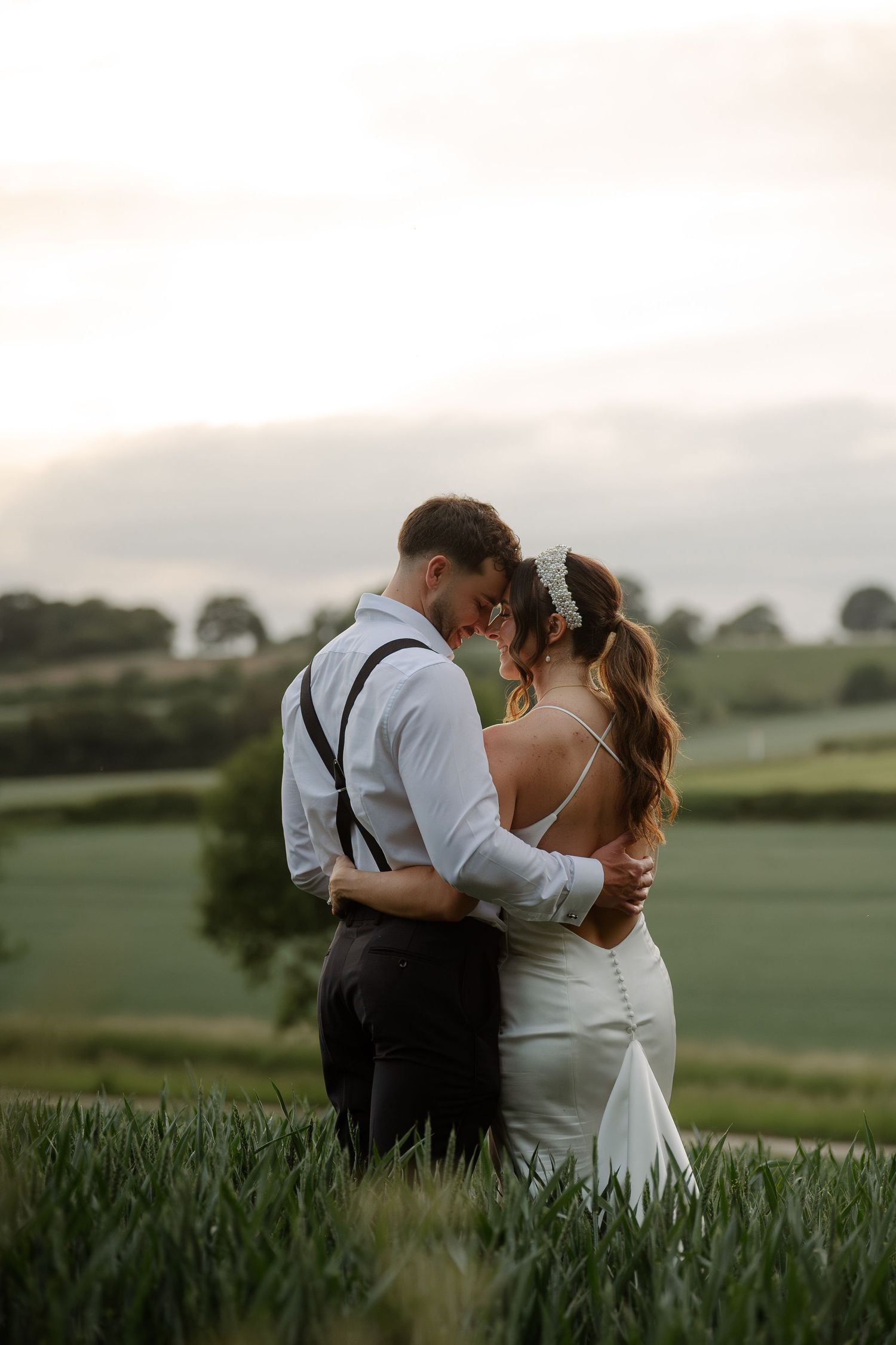 Newlywed couple sharing romantic moments in a scenic outdoor field at sunset.