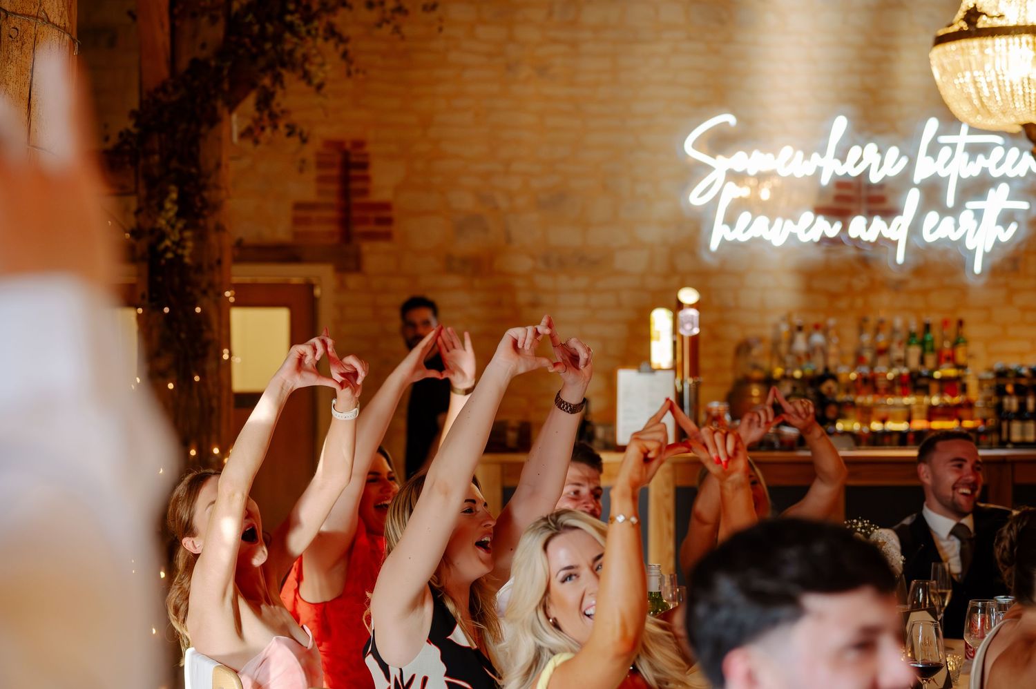 Wedding guests dance and celebrate on a crowded dance floor at an indoor reception venue with warm lighting.