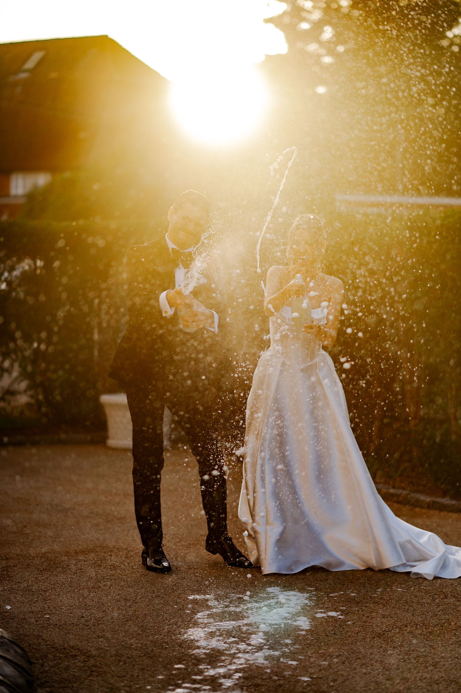 Bride and groom celebrate with champagne spray in golden sunset light on their wedding day.
