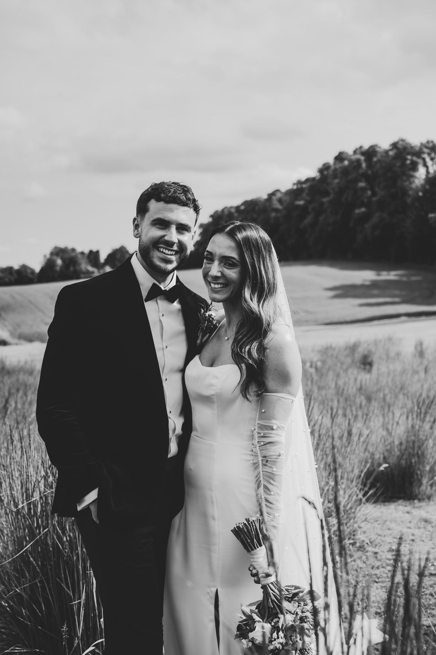 A romantic black and white photo series of a couple sharing intimate moments in a field by a lake.