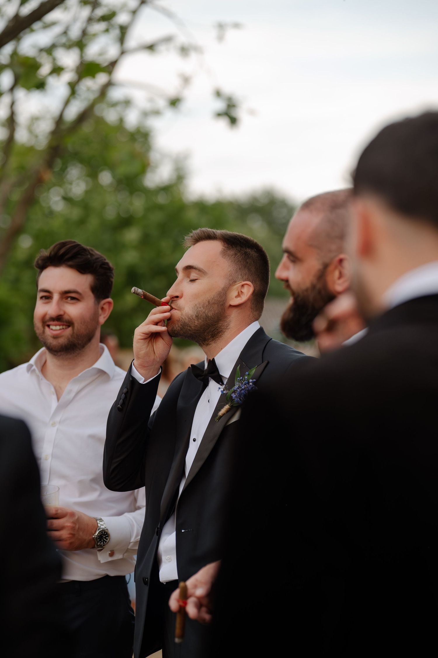 Wedding guests in formal attire gather outdoors during a celebration.