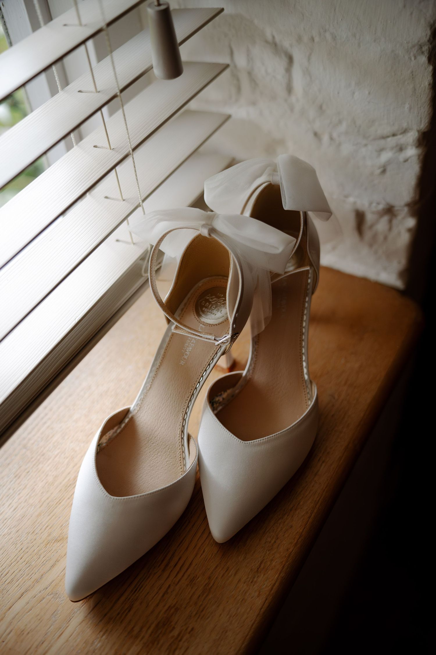 White bridal shoes placed on wooden windowsill in natural light.