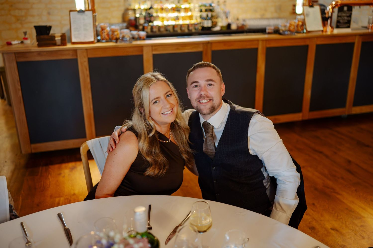 Wedding reception in a rustic venue with wooden floors and warm lighting as guests celebrate at tables.