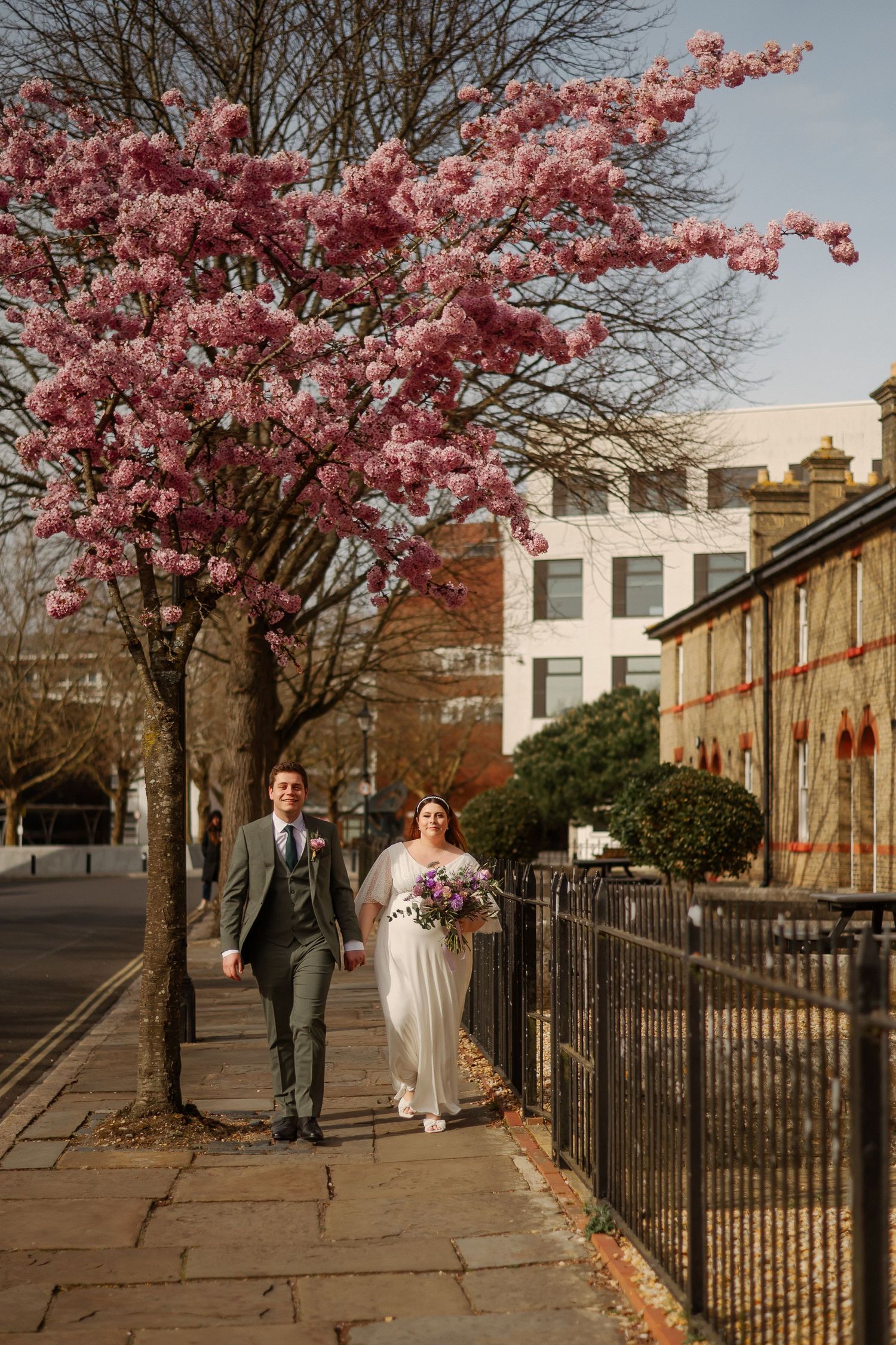 Cherry blossom tree in full bloom frames a historic stone street with iron railings and buildings in Edinburgh.