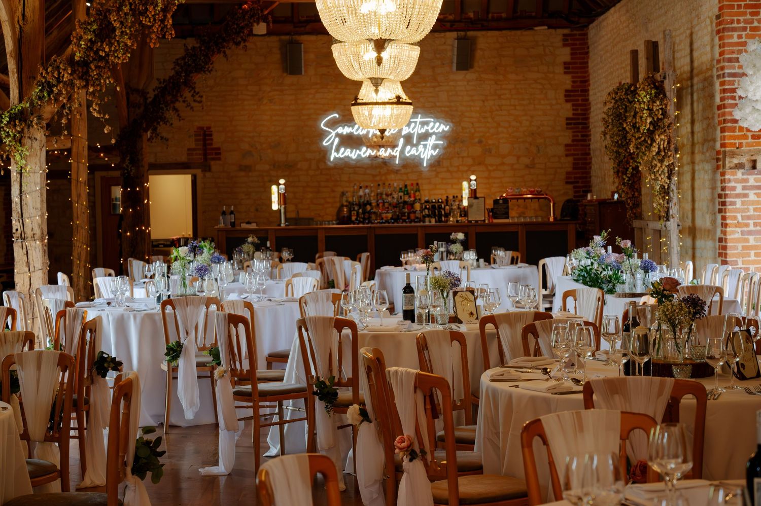 Elegant wedding reception venue with white tables, exposed brick walls, and ornate hanging light fixtures.