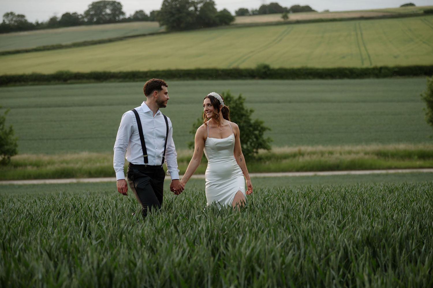 A couple walks together through a lush green wheat field on a summer day.