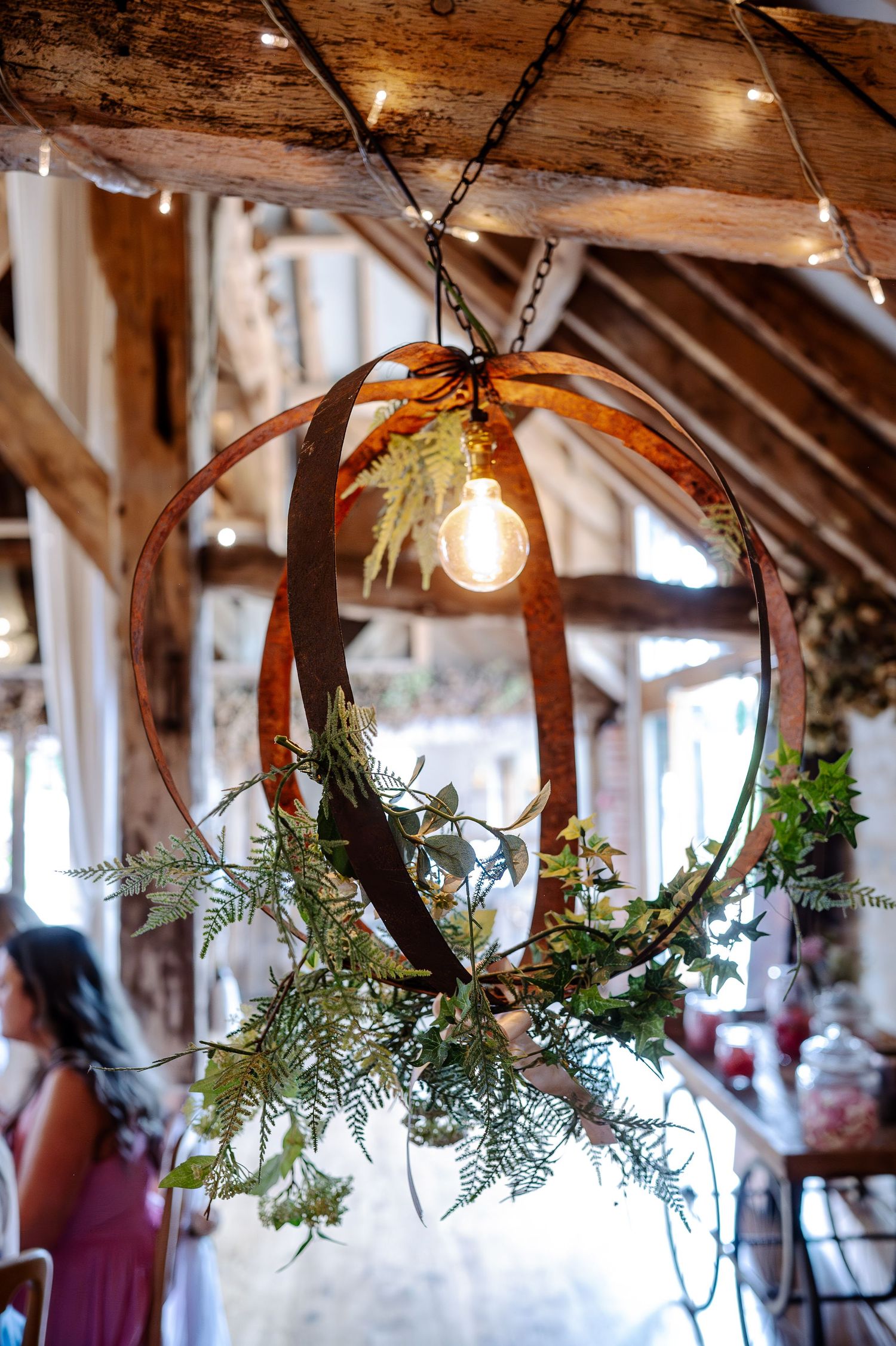Rustic wooden beams decorated with hanging greenery and glowing lights for a wedding reception.