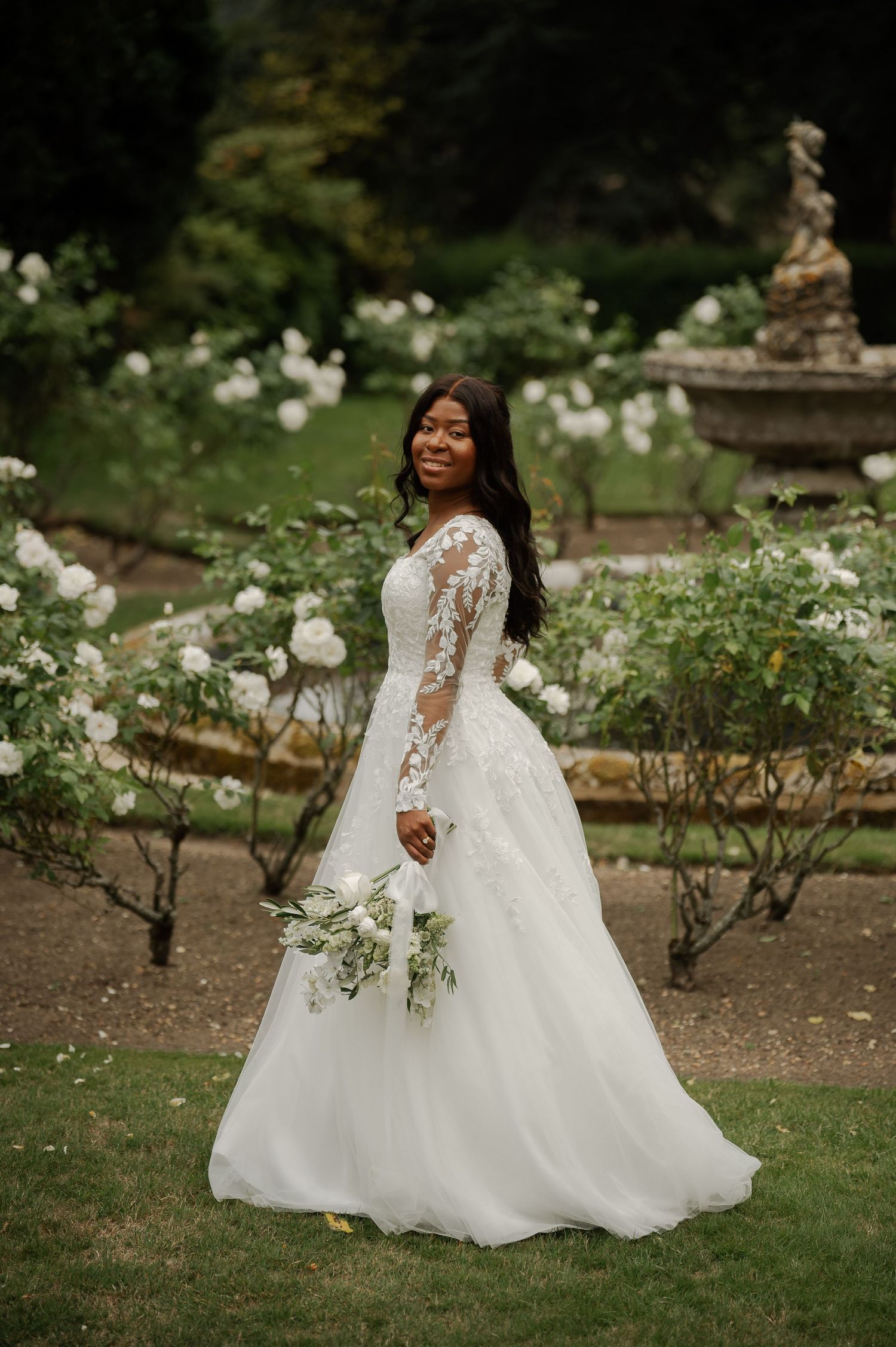 A bride in a stunning white lace and tulle wedding gown twirls joyfully in a lush garden setting.