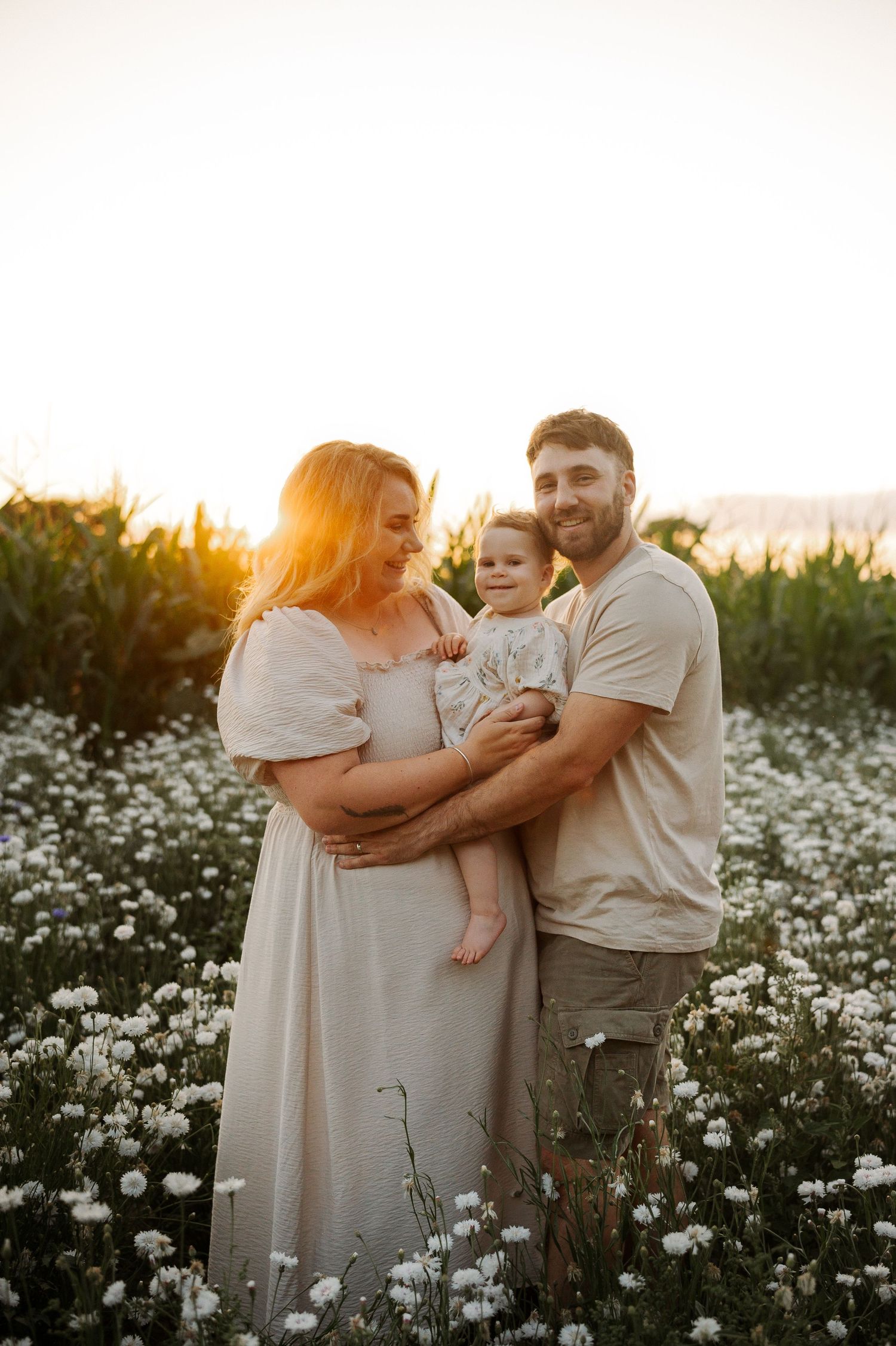 Family embracing in a field of white wildflowers during golden hour sunset.