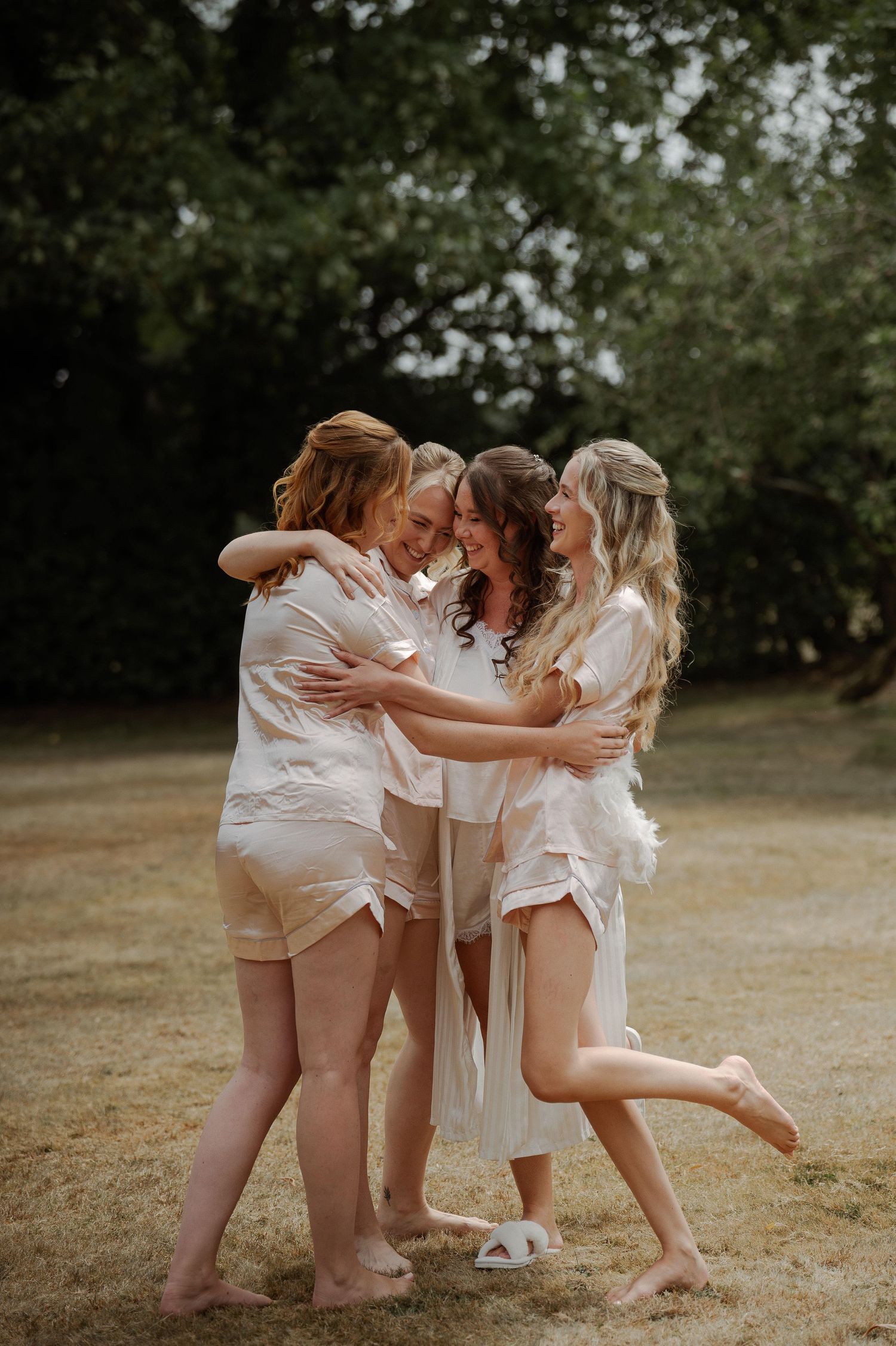 Group in white outfits sharing joyful embraces and laughter in a sunny outdoor setting.