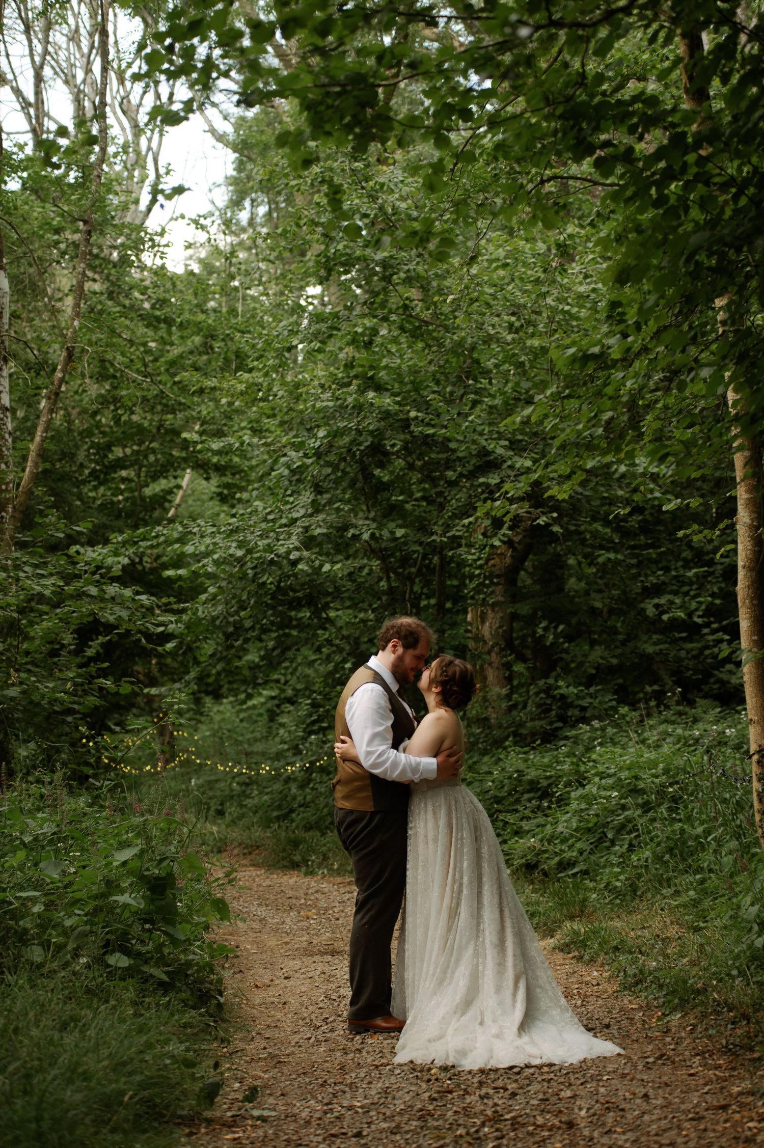 Romantic couple shares intimate moment on forest path during wedding photo session.