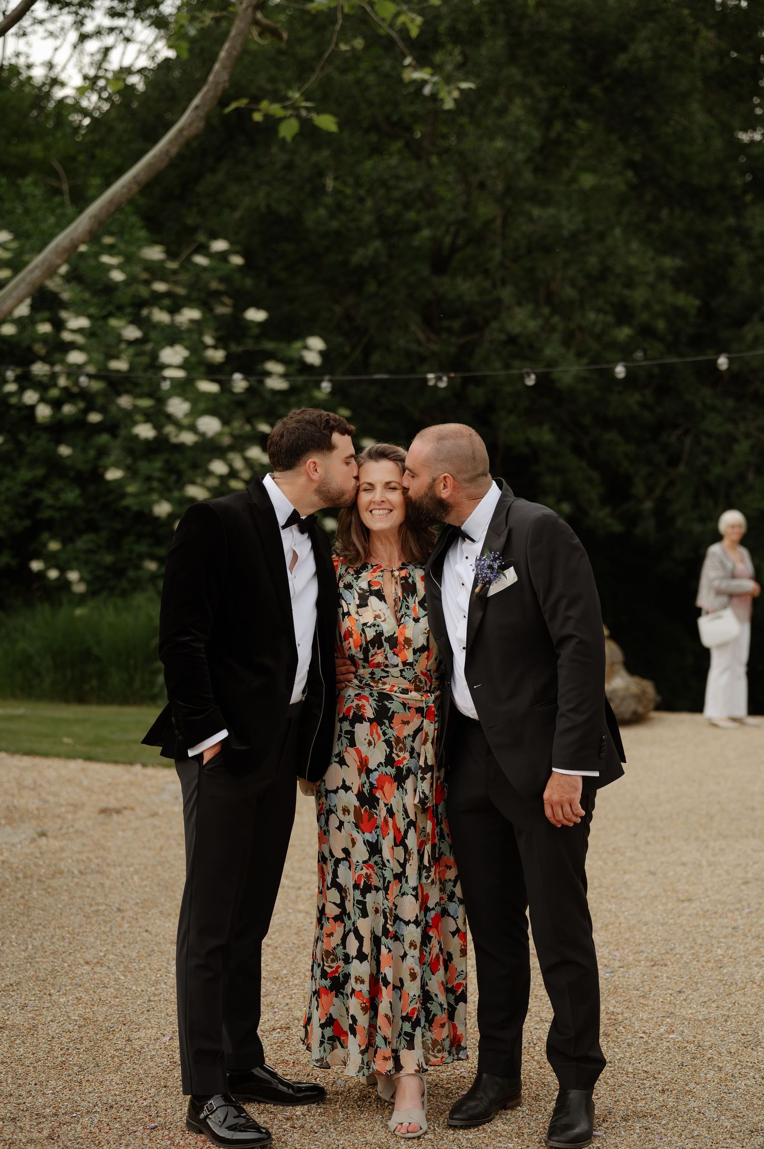 A group shares a joyful moment at an outdoor wedding celebration on a gravel path with greenery in the background.