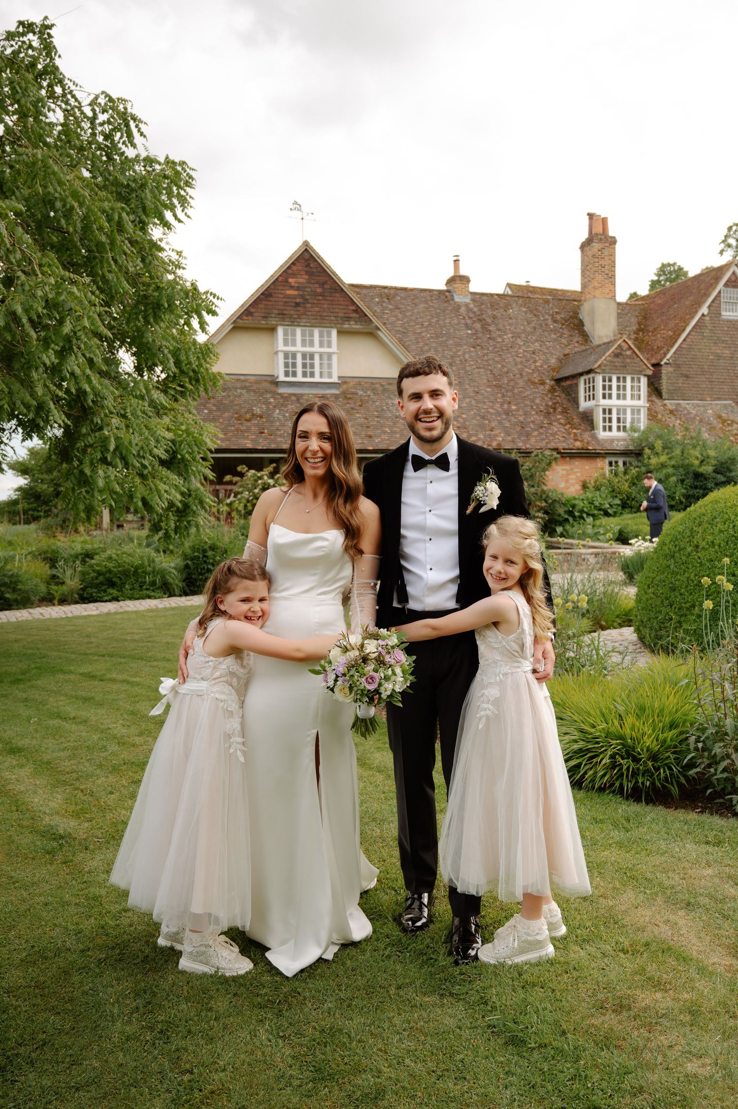 Wedding party poses on a grassy lawn in front of a traditional English countryside home.