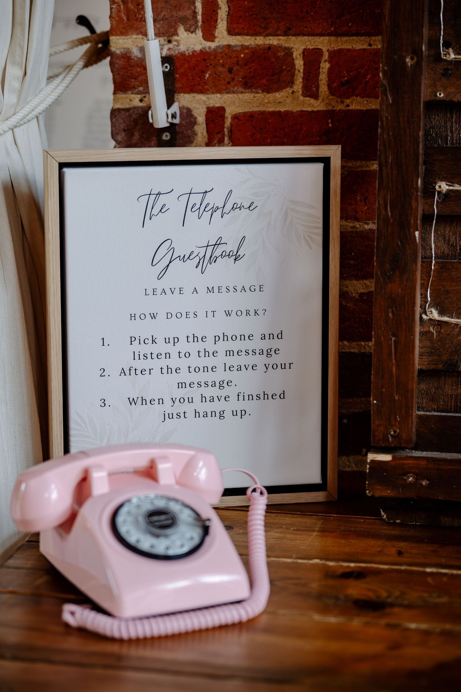 Vintage pink rotary telephone display with instructional signage against rustic brick wall.