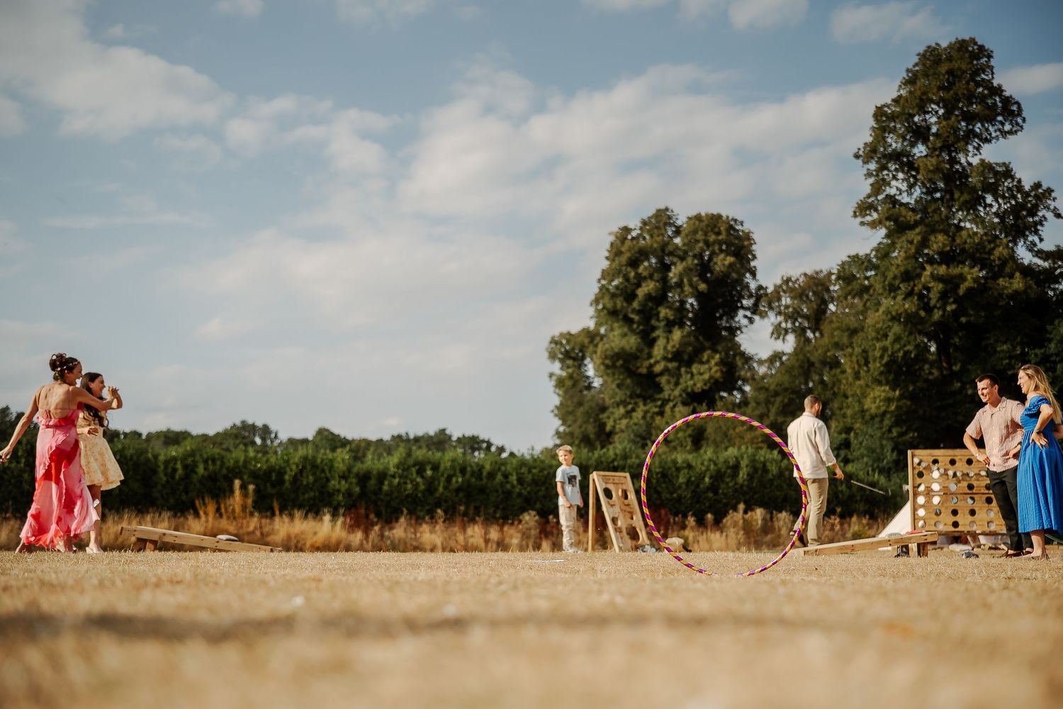 Guests playing lawn games including hula hoop and giant Connect Four at an outdoor summer wedding reception.